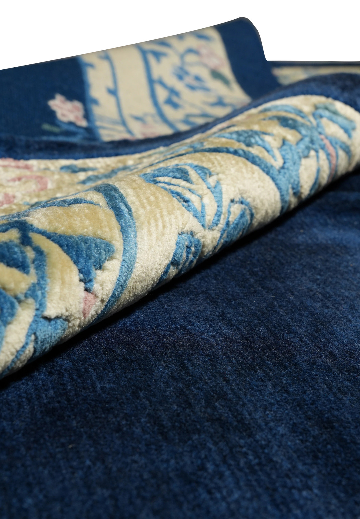 Rolled view of navy blue Beijing Art Deco rug highlighting plush wool and floral border.