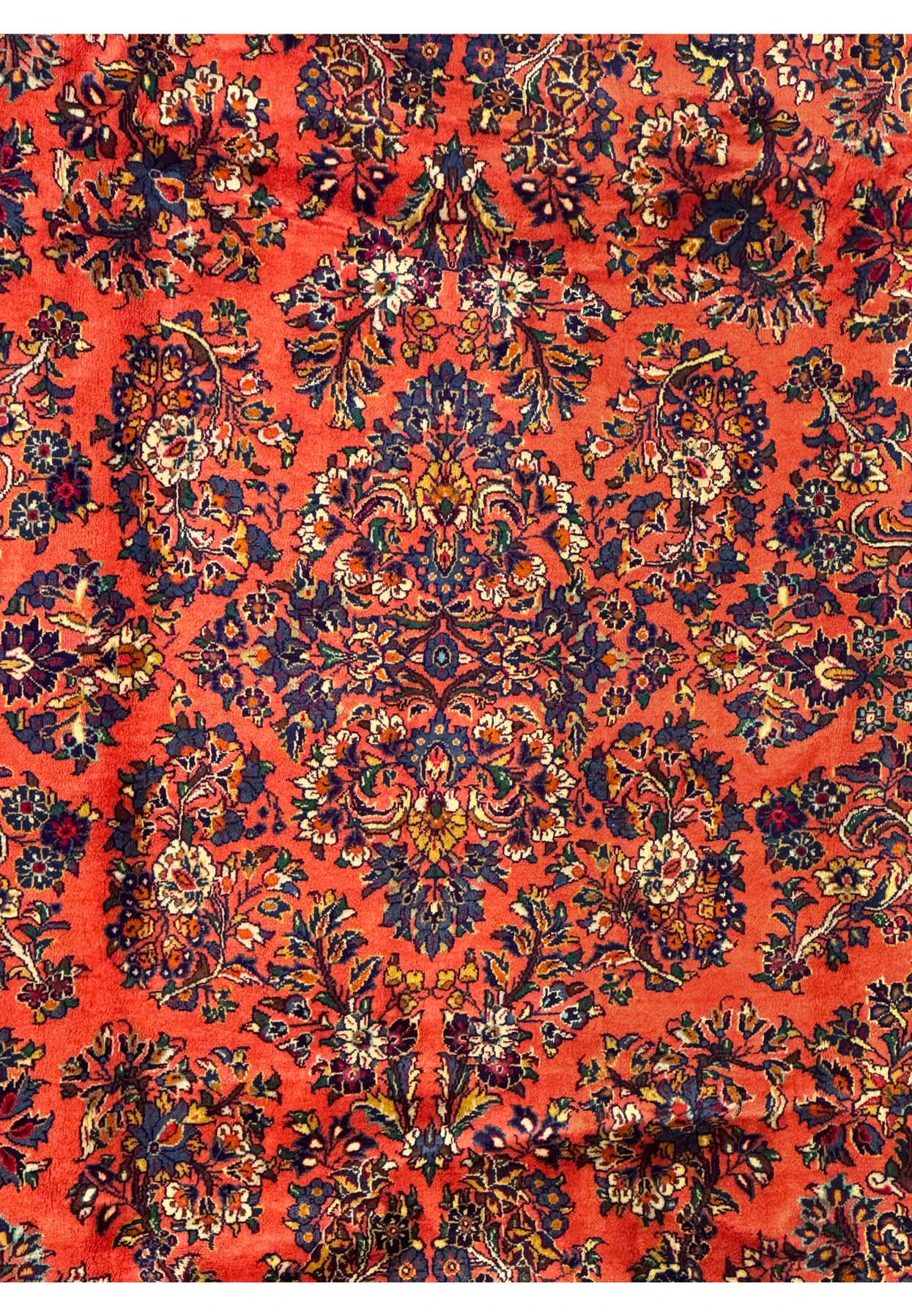 Persian Sarough rug medallion detail with intricate navy, ivory, and burgundy floral motifs on a coral wool background, fine hand-knotted design.