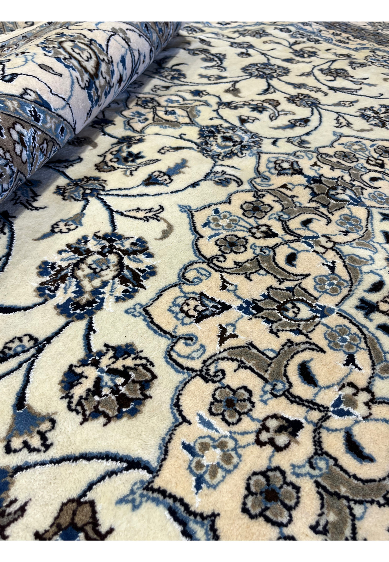 Detailed rolled view of 10x13 Nain 9LA Rug displaying contrast between ivory field, taupe borders, and blue floral vines.