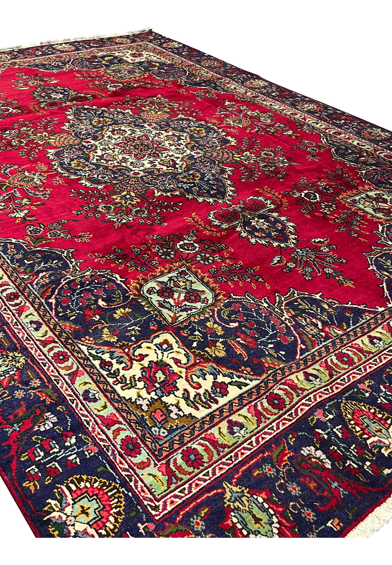 Angled view of 8'5" x 12'9" Persian Tabriz rug showing red field and navy corners