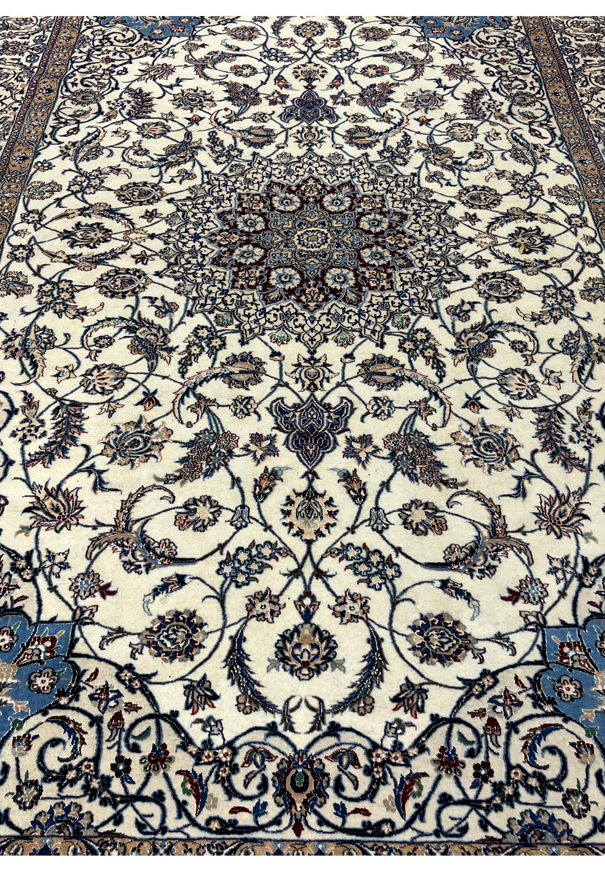 Top-angle view of a Persian Nain 4 LA Habibian rug showing luminous ivory field, navy floral motifs, and ornate royal blue corner designs.