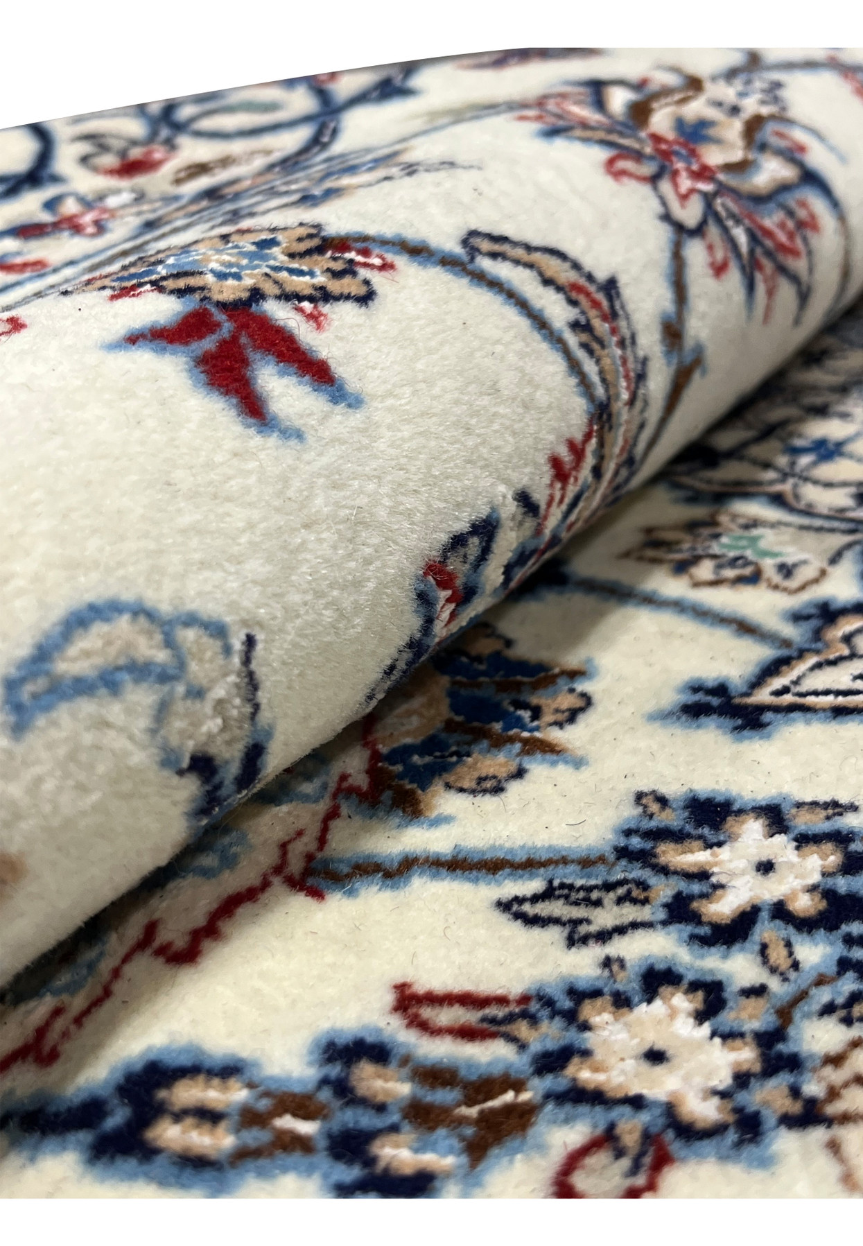Rolled section of Persian Nain 4 LA Habibian rug highlighting its ivory wool pile, fine silk sheen, and detailed floral motifs in red, blue, and beige.