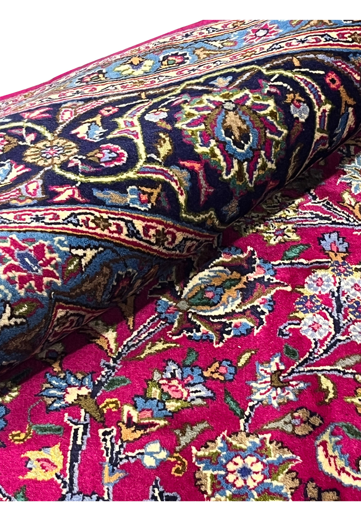 Rolled view of semi-antique Mashad rug highlighting red field, navy border, and intricate floral motifs.
