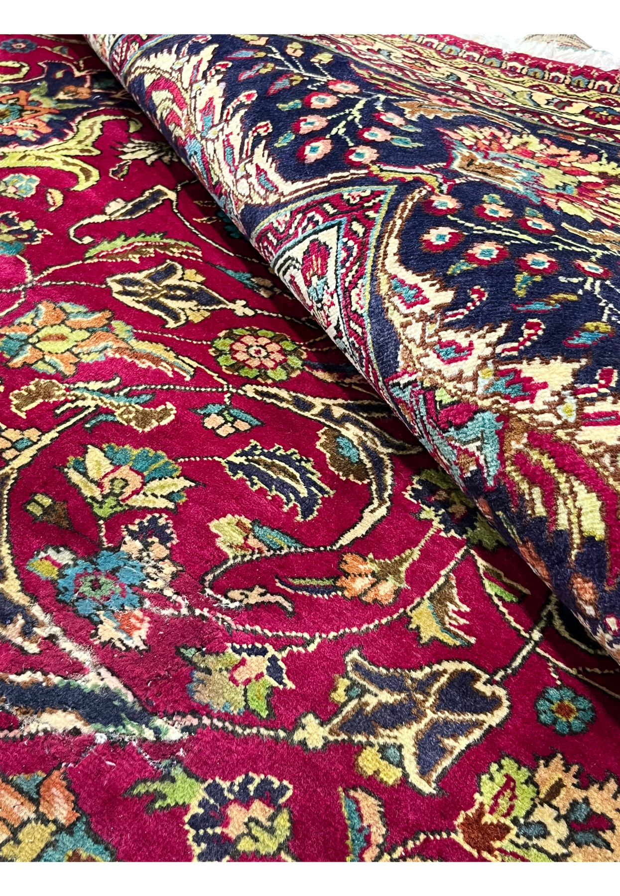 Close-up folded view of the vintage Persian Tabriz rug revealing the red field, floral patterns, and plush wool pile texture on a cotton foundation.