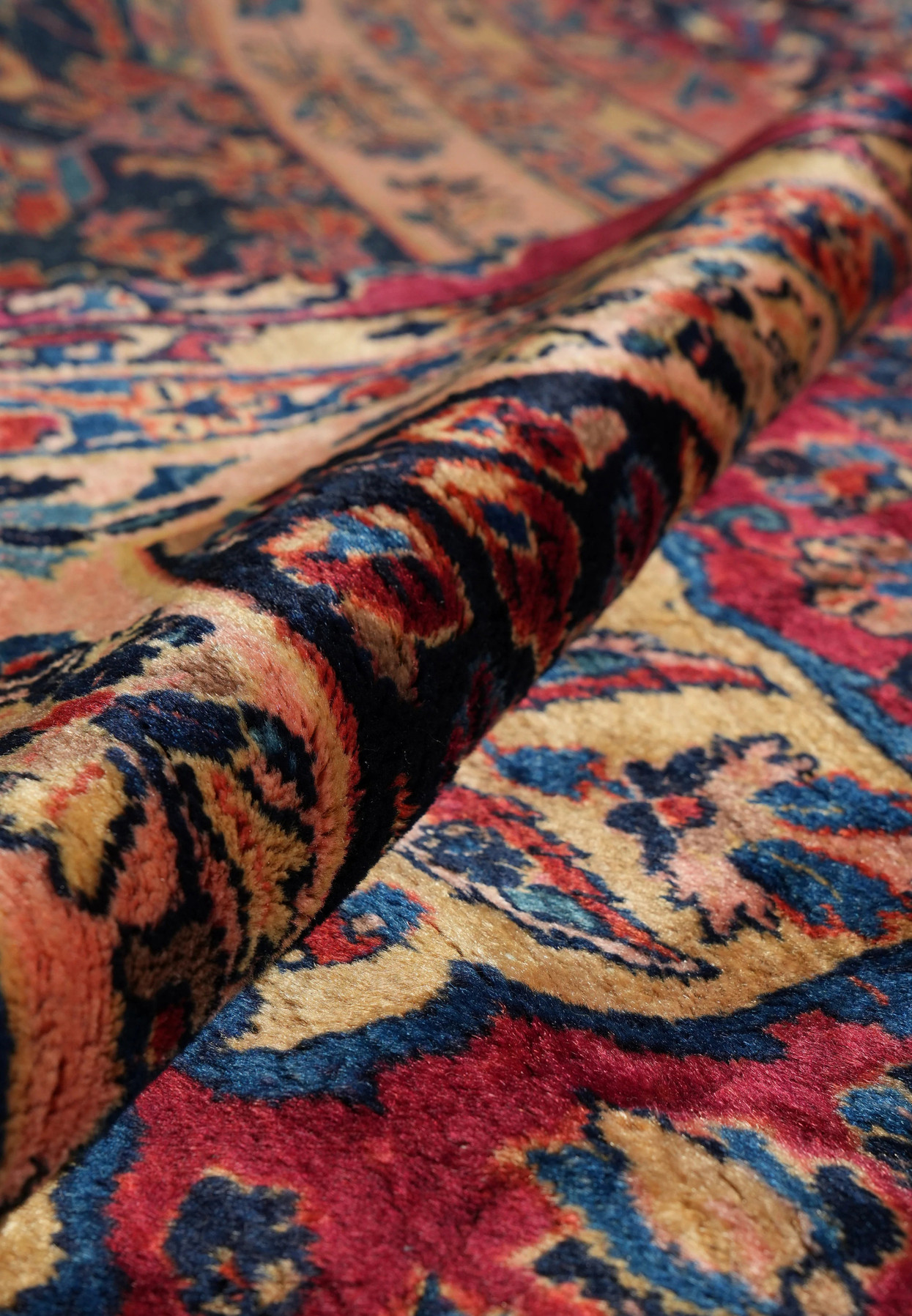 Rolled view of 1930s Persian Kashan rug showing fine wool pile, rich red and navy tones, and intricate hand-knotted floral motifs