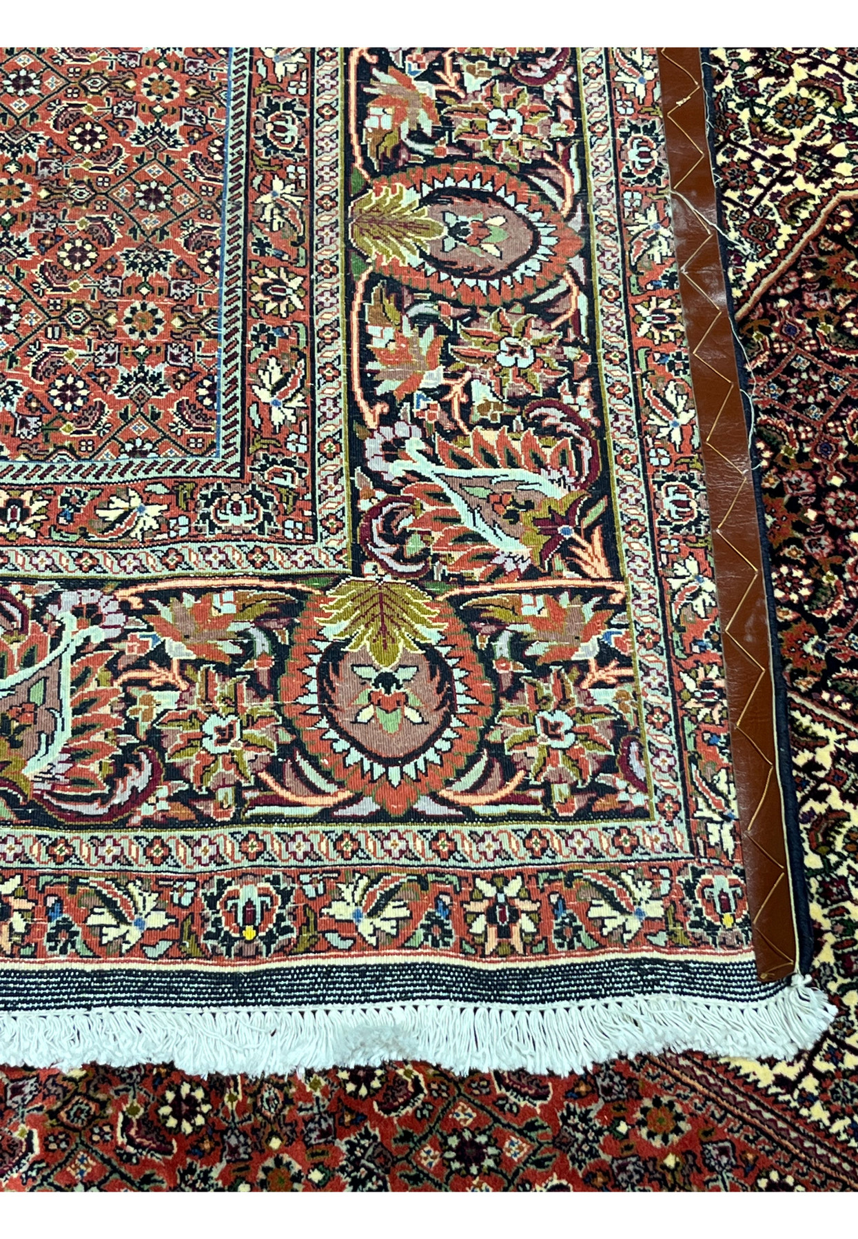 Close-up of the Bijar Persian Iron Rug border showing detailed floral motifs, rich brick red tones, cream fringe, and dense Kurdish weaving.