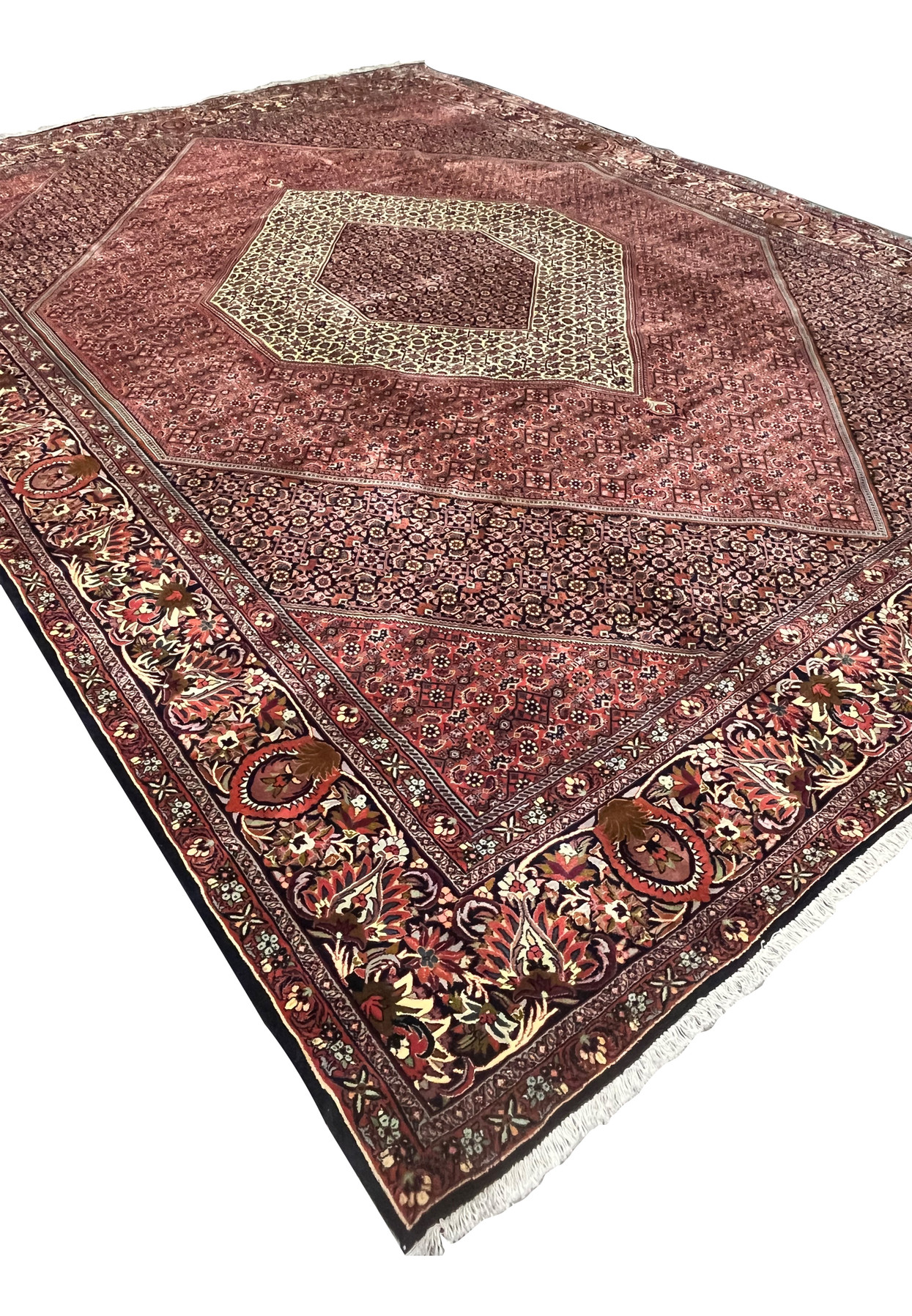 Angled view of a large Persian Bijar iron rug showing diamond medallion layout, dense red field, and heavy wool structure