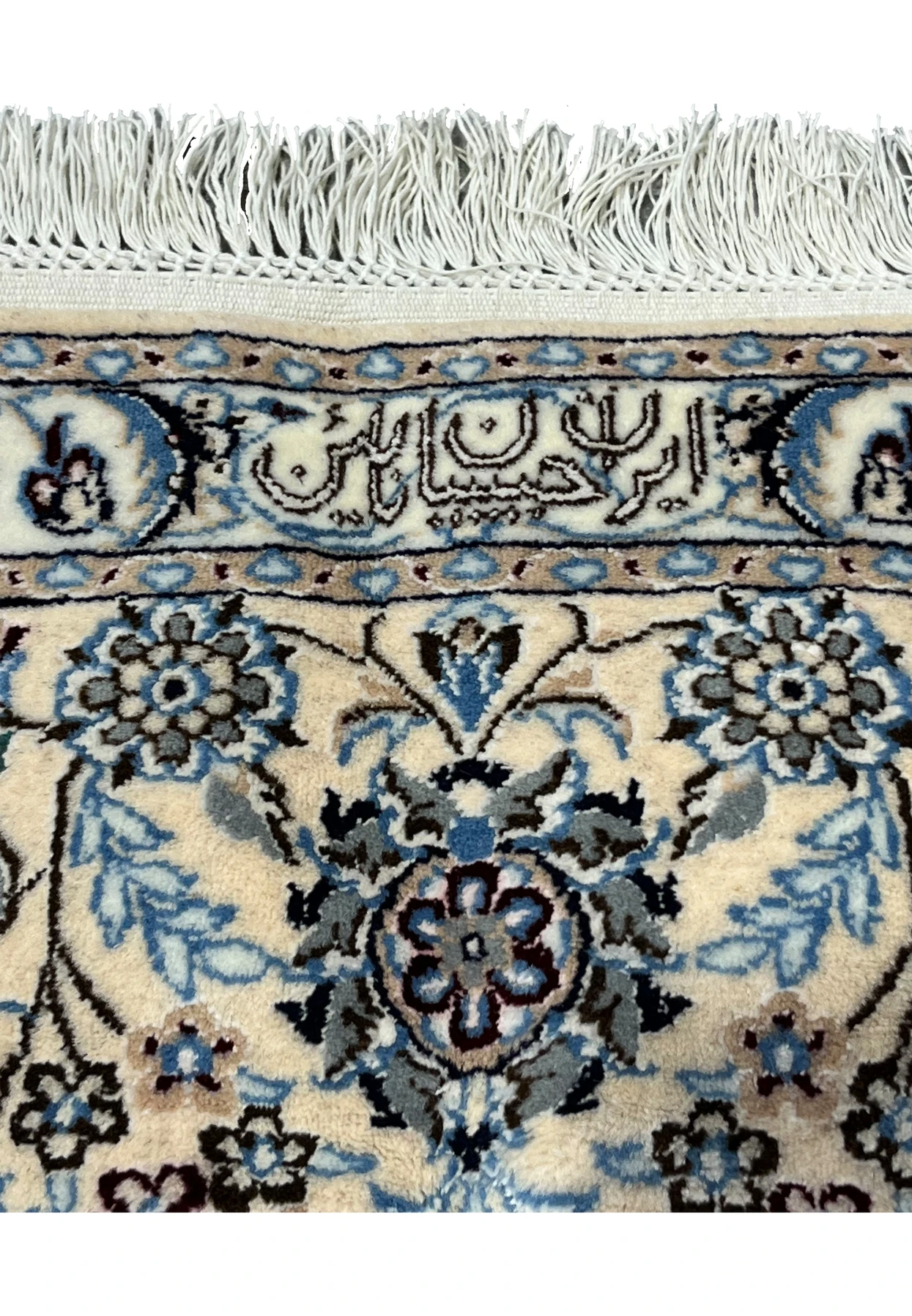 Close-up of the woven Habibian signature cartouche on a Persian Nain rug framed by floral motifs and finished ivory fringe