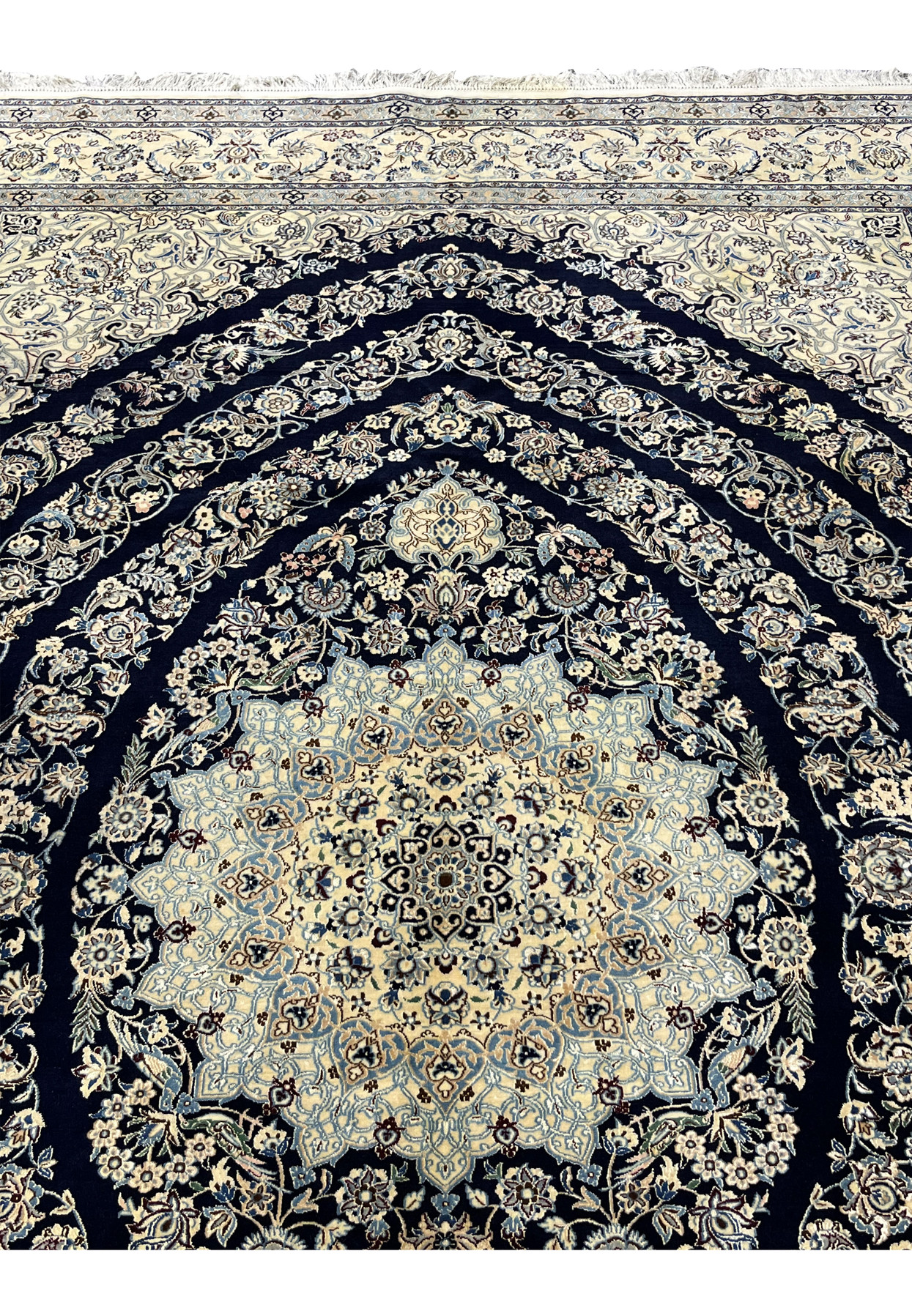 Upper section of Persian Nain 6 La rug showing navy field with scrolling floral vines and silk highlights near the top border