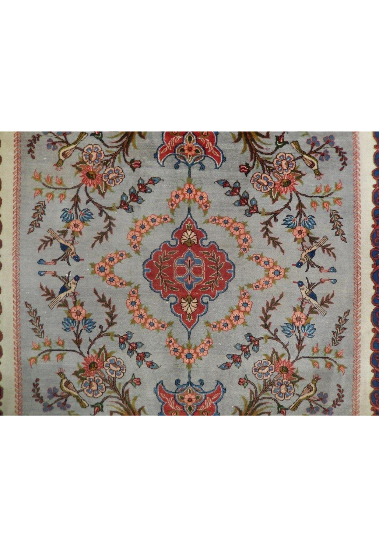 Close-up of the central medallion on a grey Persian Isfahan rug showing floral detailing, muted red tones, steel blue vines, and ivory outlines
