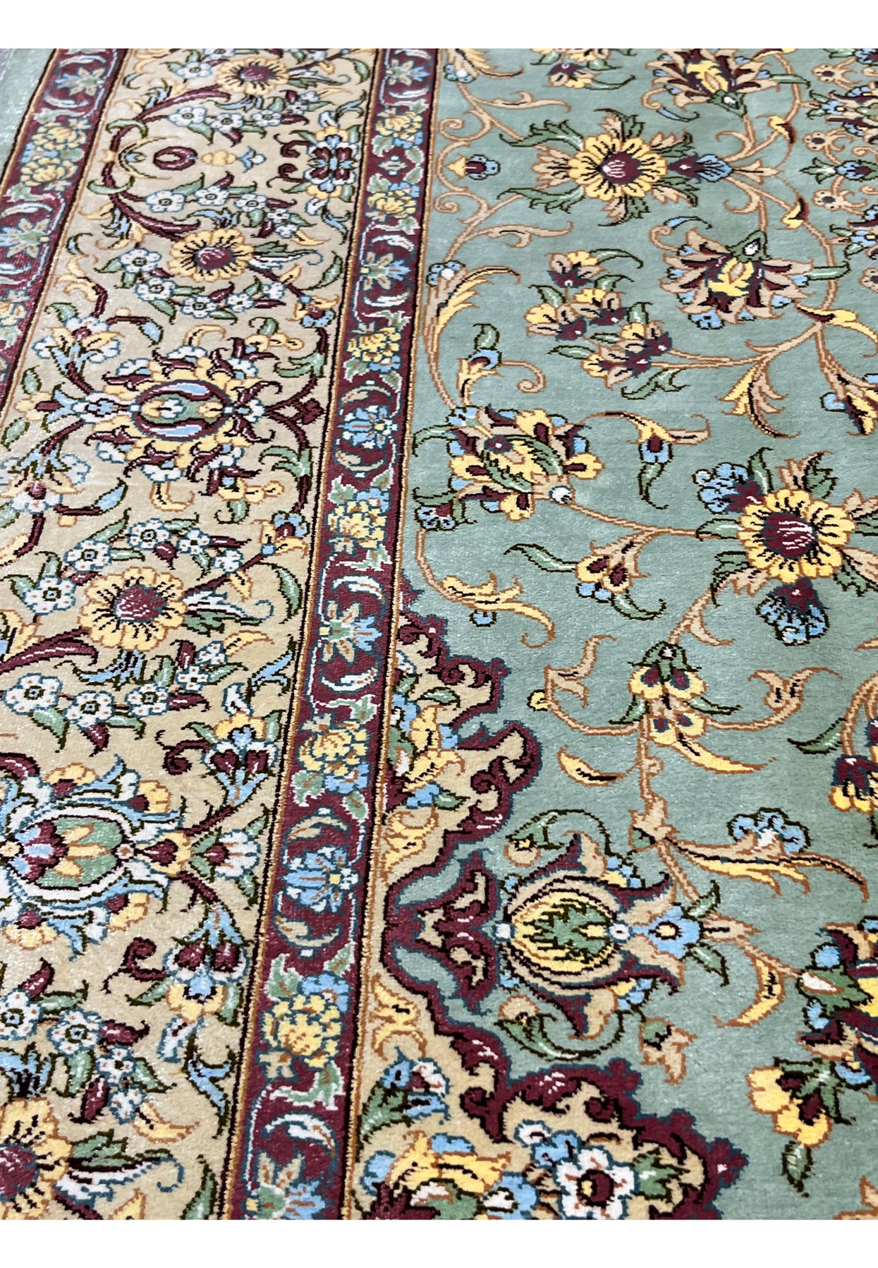 Angled side view of Persian Qum pure silk rug highlighting silky texture, tight knot structure, sage green field, and scrolling floral design
