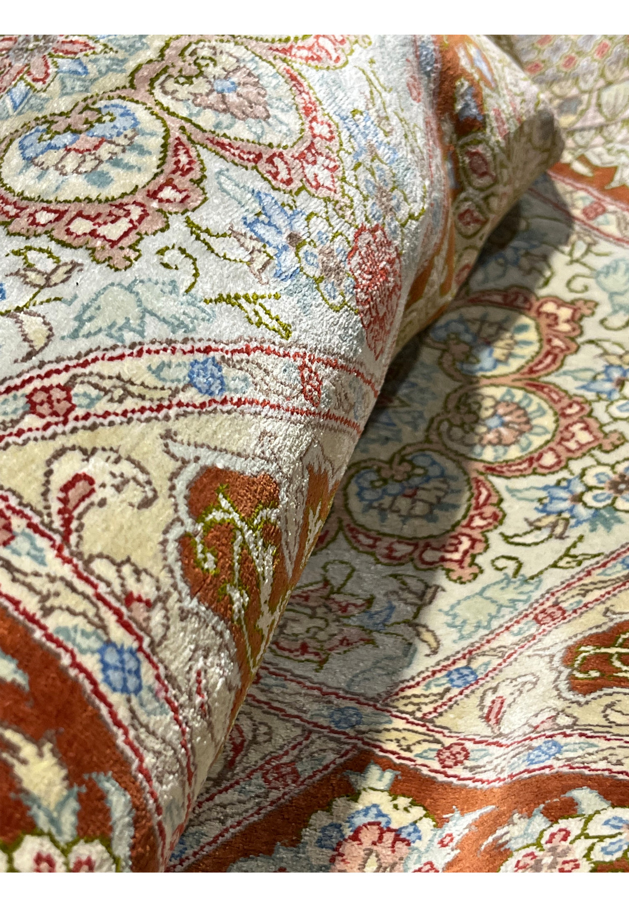 Close-up of rolled signed Amjadi Persian Qum silk rug showing tight structure, fine silk foundation, and high-definition weaving