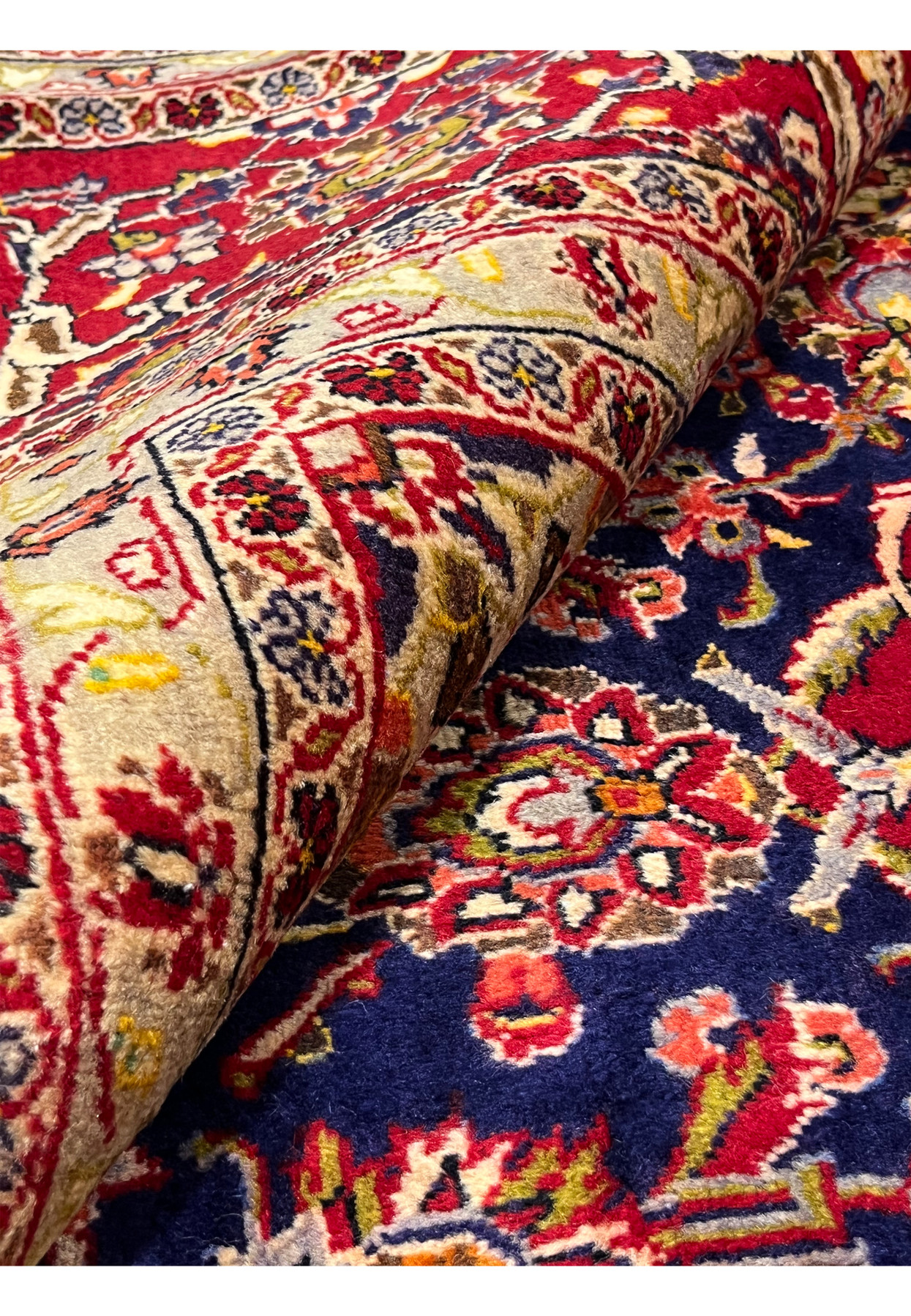 Rolled Persian Isfahan rug emphasizing dense pile, flexible structure, rich navy and red colors, and fine traditional craftsmanship