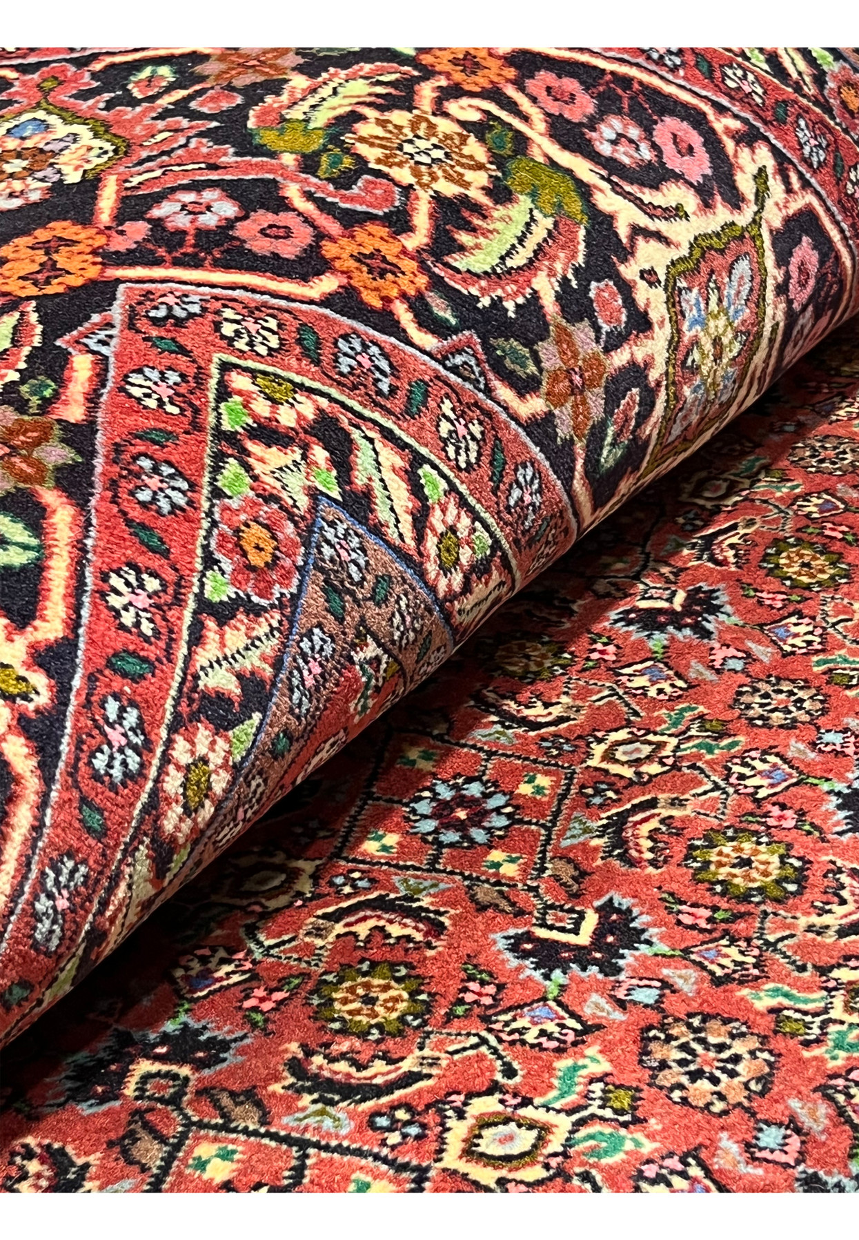 Persian Bijar all-over rug partially rolled to display rich terracotta field, navy border, and intricate floral motifs