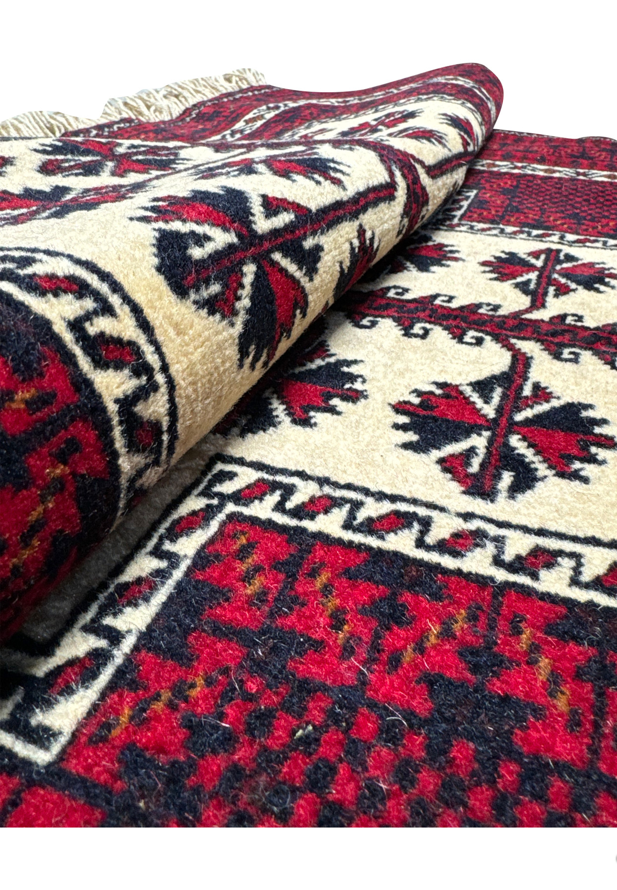 Hand-knotted Persian Baluch tribal rug rolled showing low 0.3 inch wool pile and ivory cotton fringe