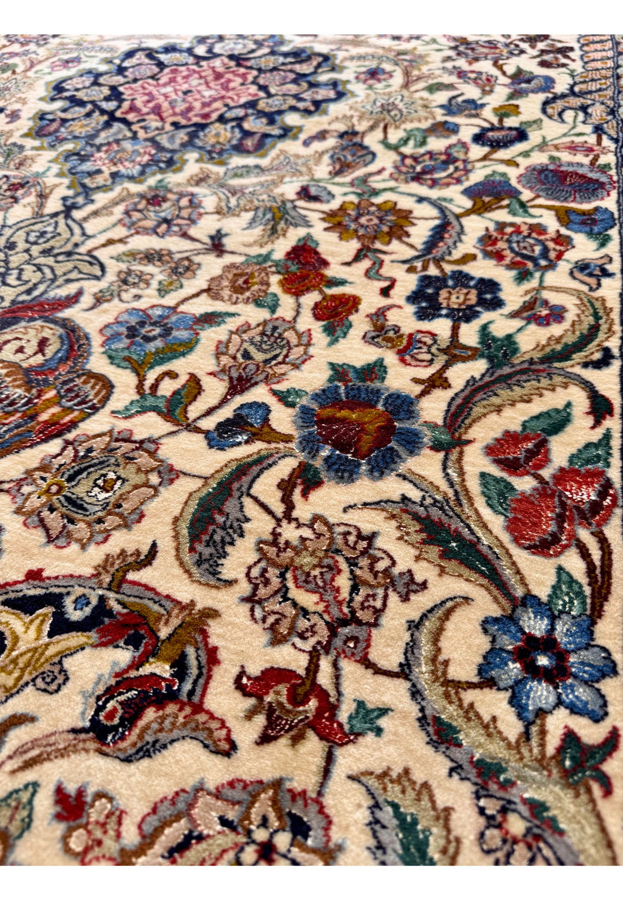 Macro detail of one floral cluster showing rose buds, lotus heads, and curling vines drawn with the precision typical of fine workshop Isfahan weaving