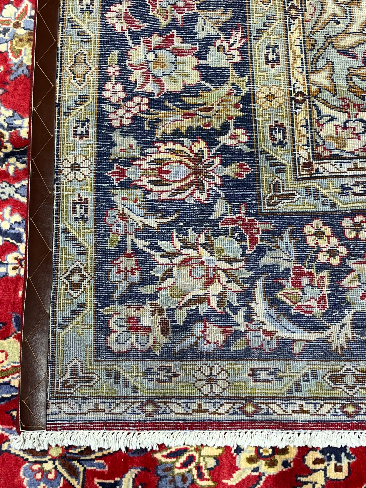 Backside corner of authentic Persian Isfahan rug showing dense knot structure on cotton foundation