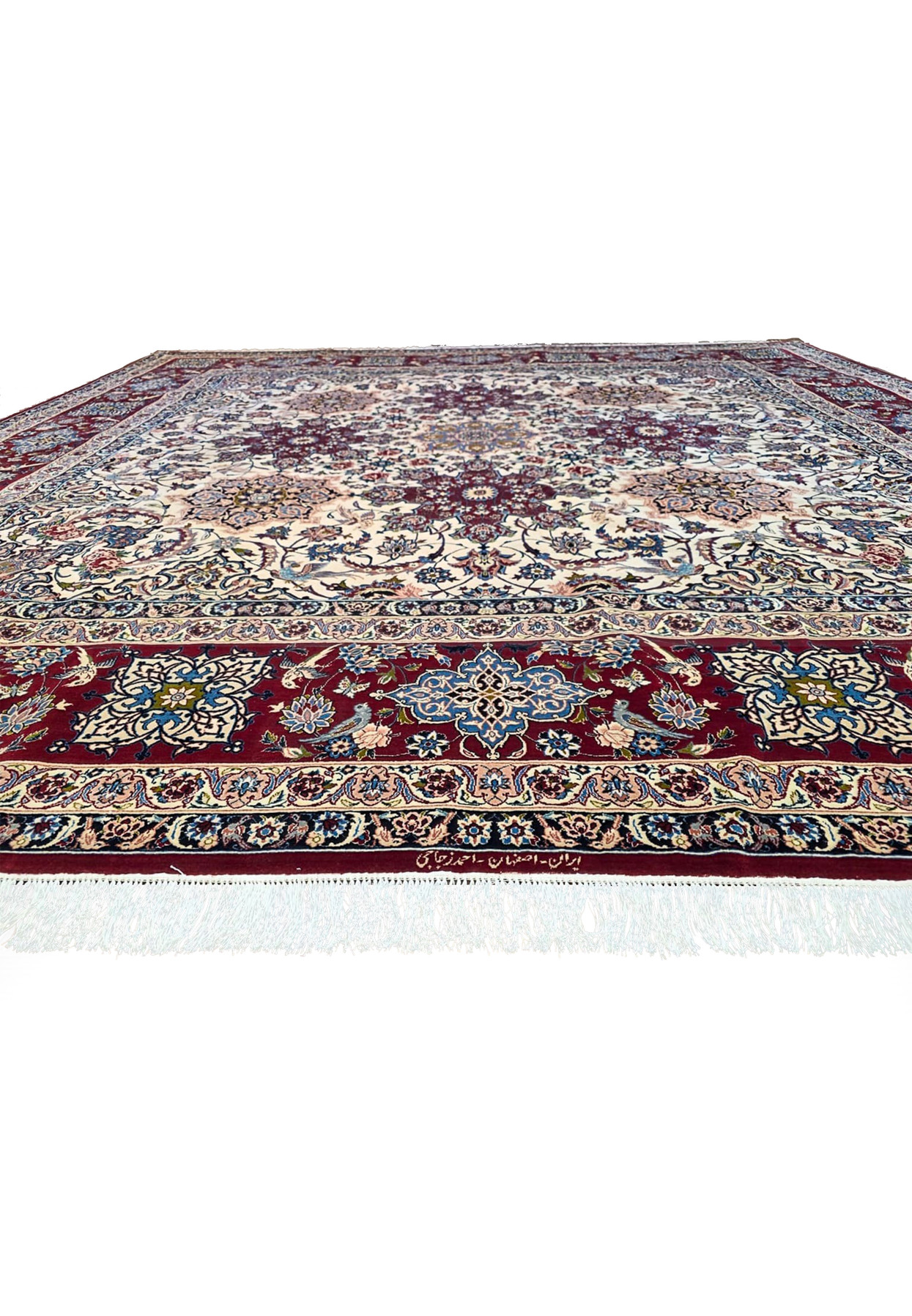 Persian Isfahan square rug shown from a low angle, ruby border meeting ivory field with navy guard stripes