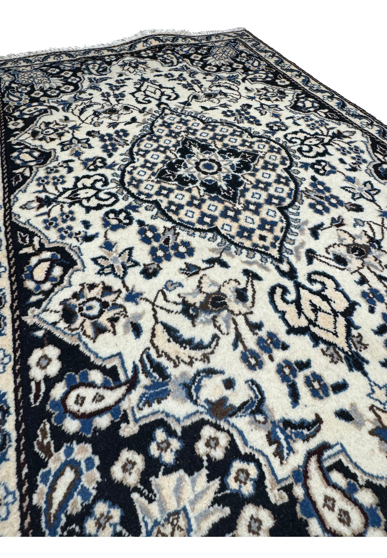 Angled studio view of Persian Nain rug from the foot end, layered floral medallion glowing against ivory and navy palette