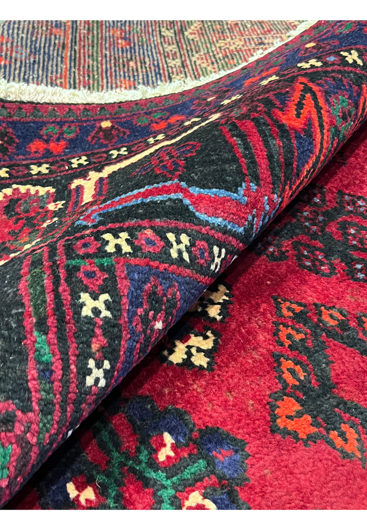 Rolled corner of 10x13 Persian Meymeh rug showing full thick pile, dense knot count, cherry red and navy palette