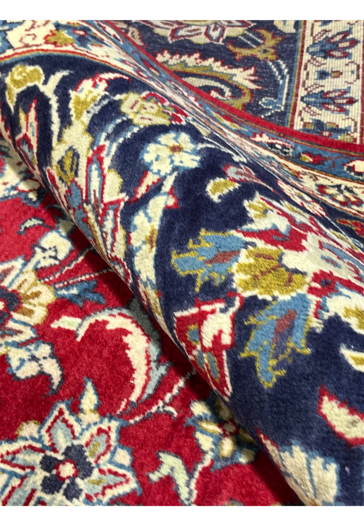 Rolled corner of 10x14 Najafabad rug, full thick wool pile, navy border curling over cherry red field, hand-knotted