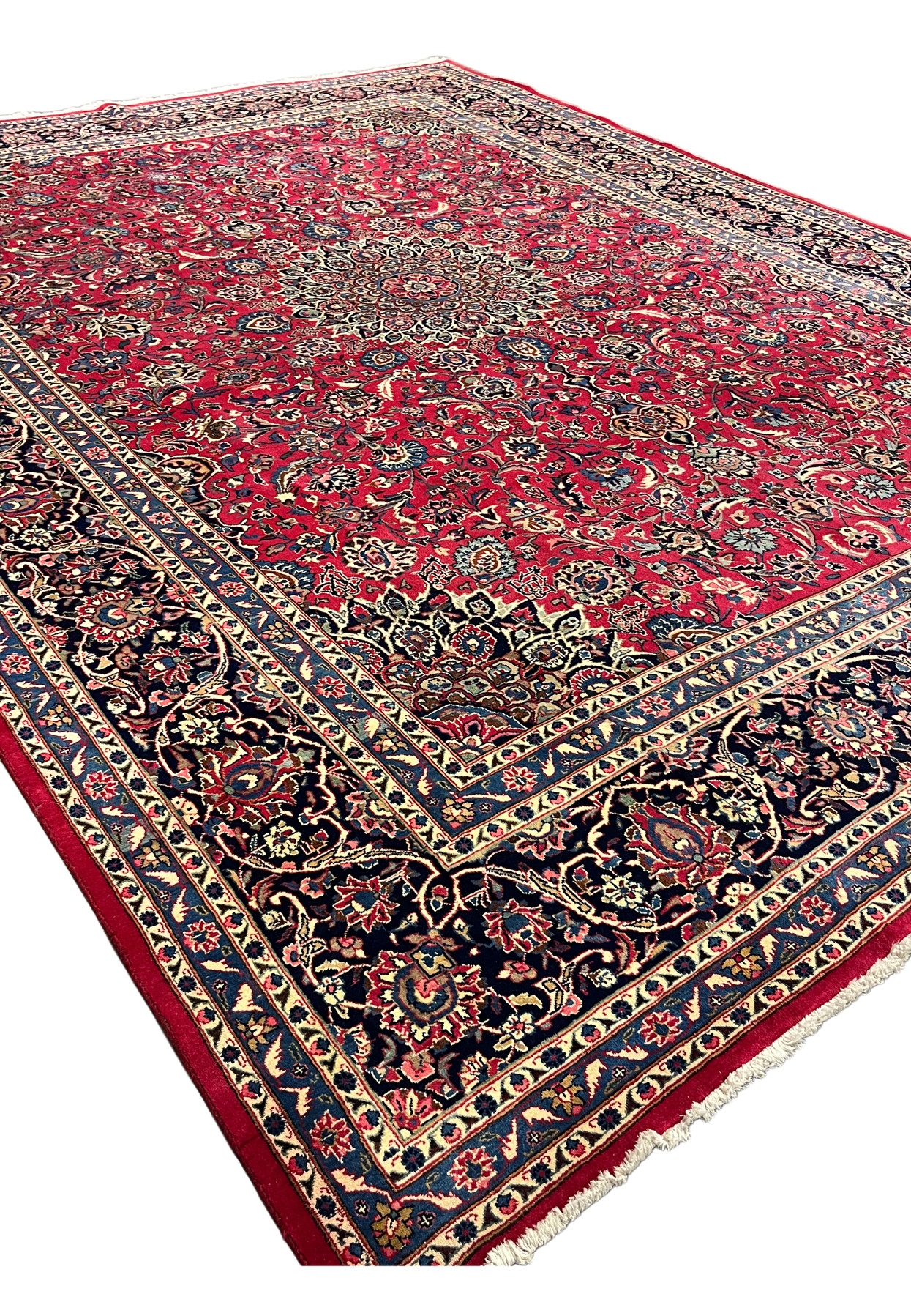 Angled view of hand knotted Persian Mashad rug, cherry red medallion field with navy border and full wool pile