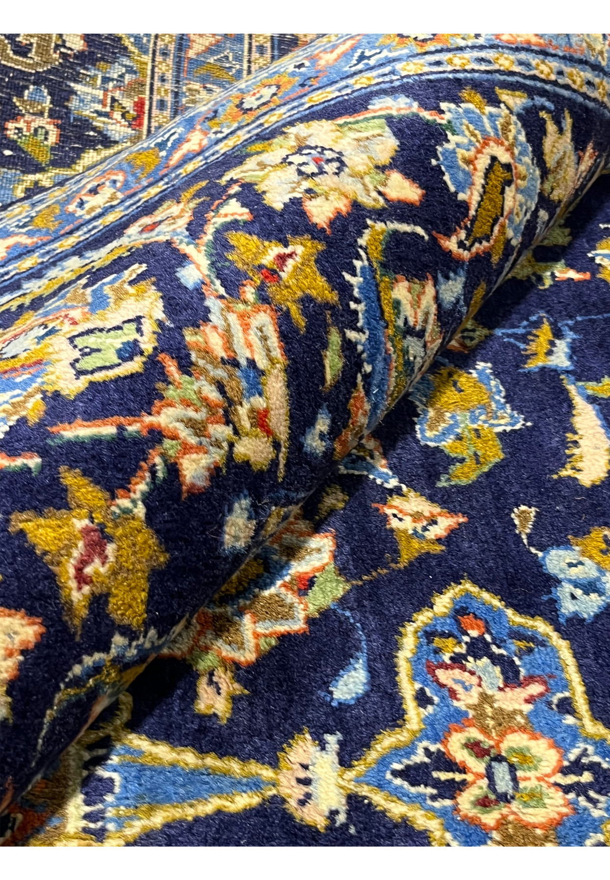 Rolled view of 8x11 navy Persian Kashan rug showing soft hand-knotted wool pile and border detail