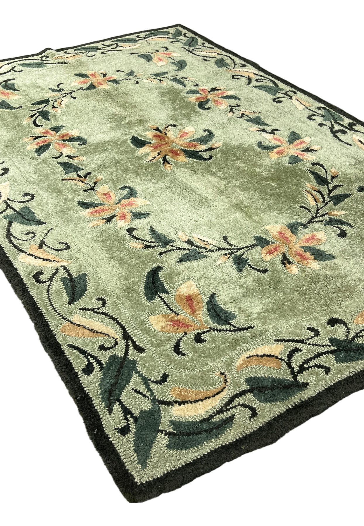 Angled view of vintage hand-hooked floral rug with sage green field and dark green wrapped edge