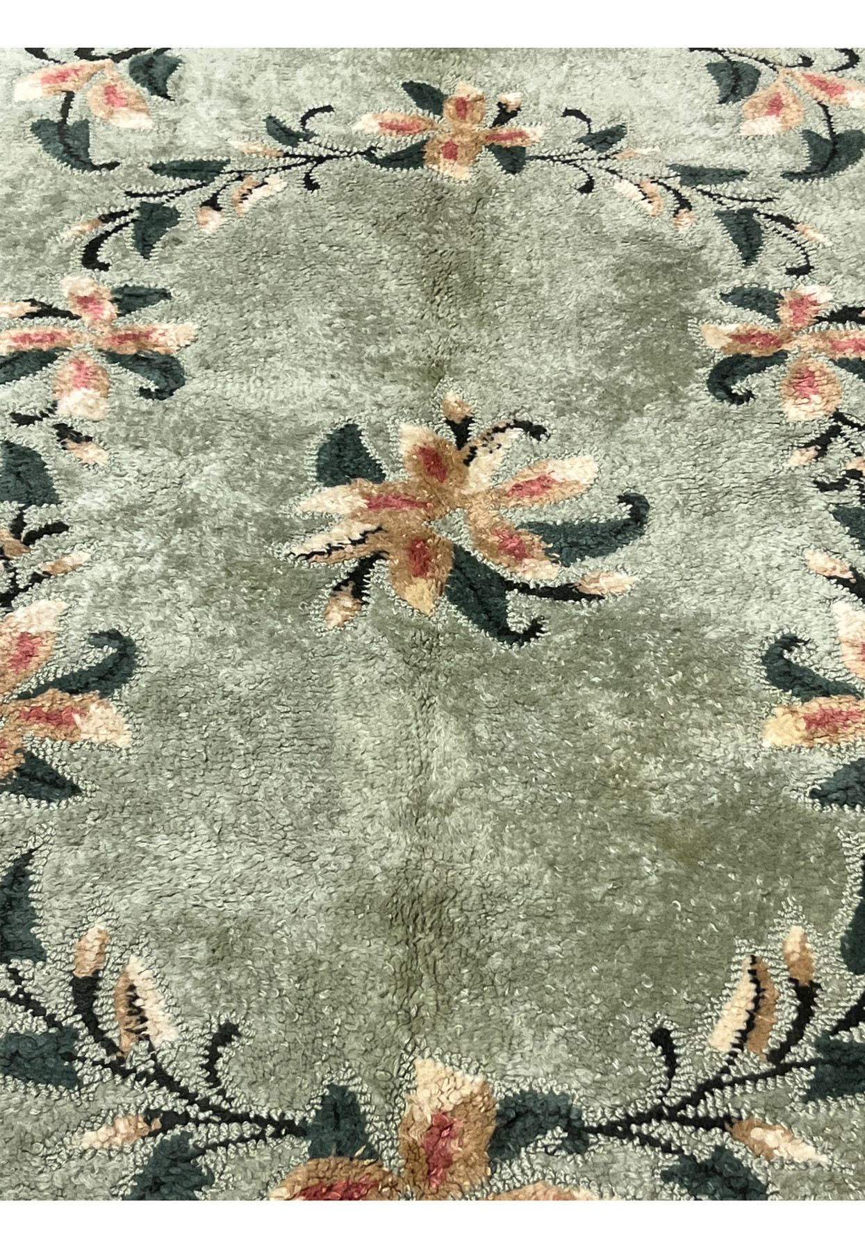 Center detail of hand-hooked rug with a peach and rose flower spray on a celadon green ground