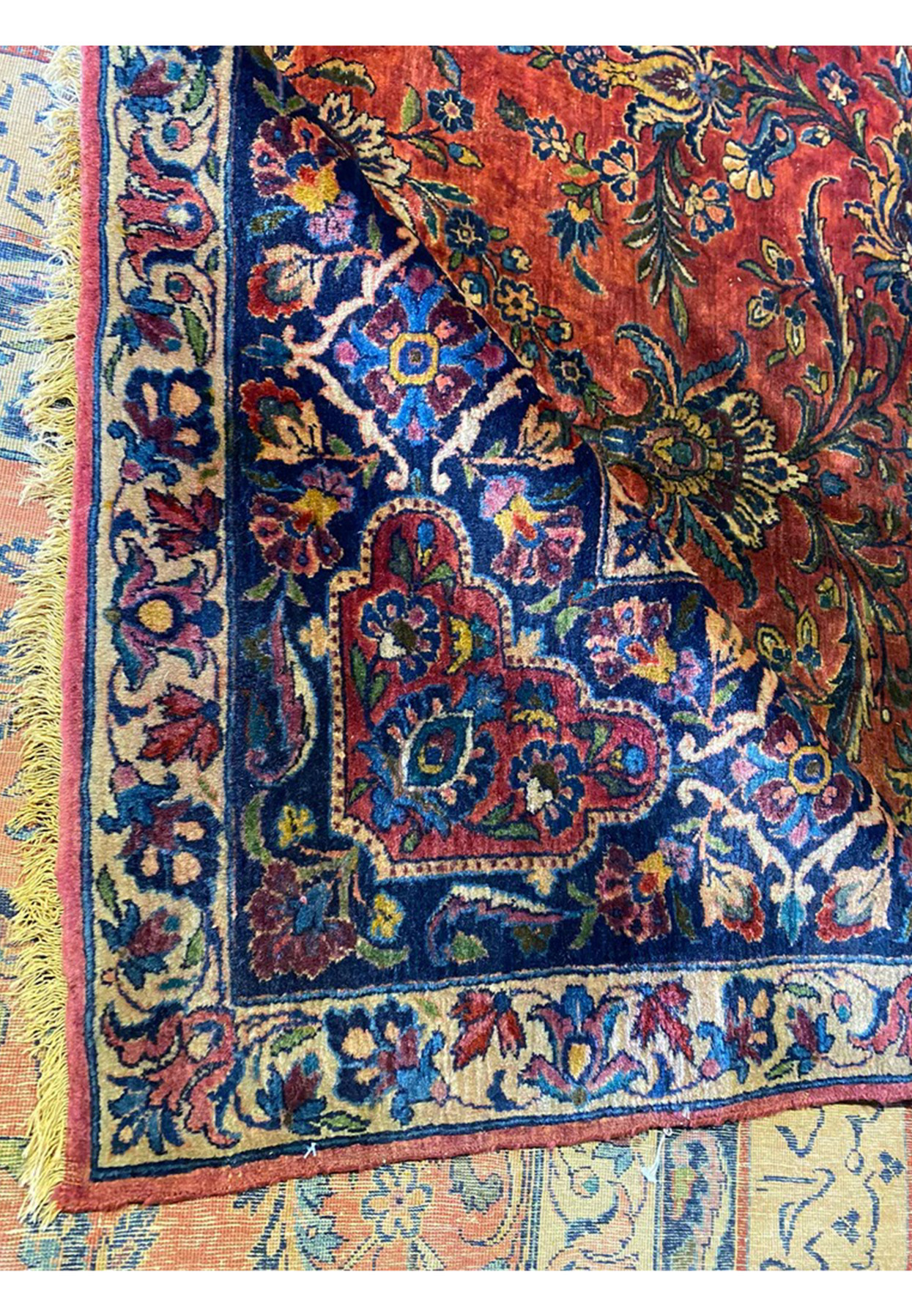 Folded edge of antique Persian Sarough rug showing navy border and ivory floral guard stripe