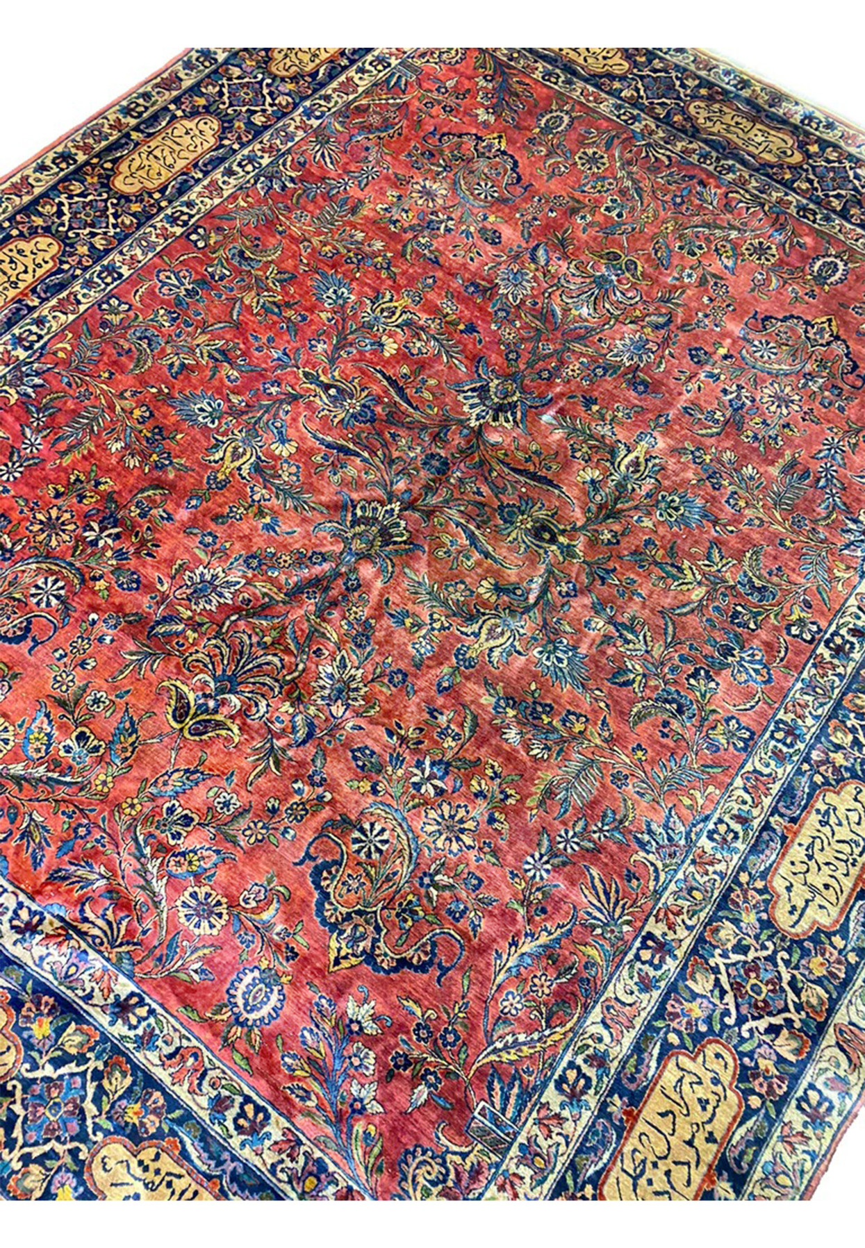 Angled view of antique Persian Sarough rug, red floral field framed by navy poetry border