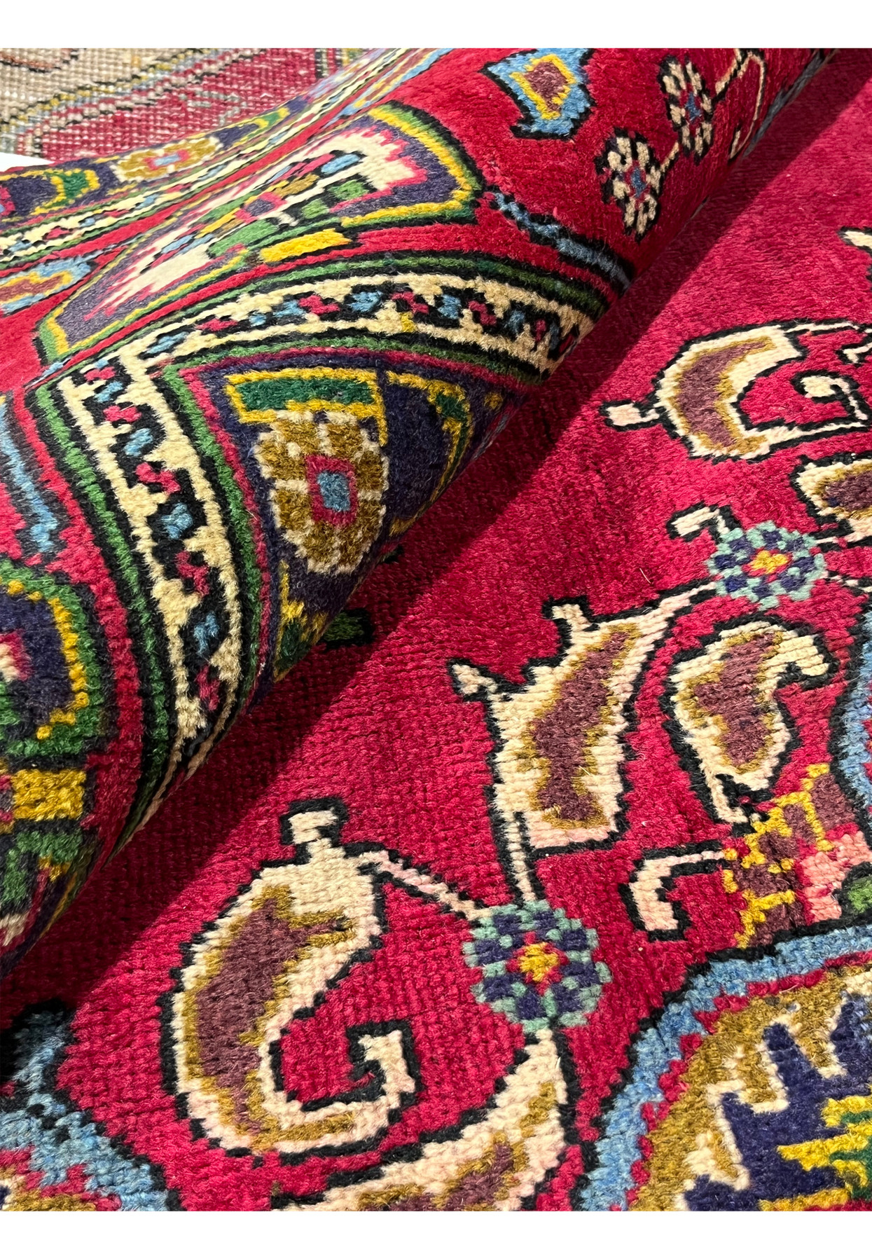 Rolled view of Persian Tabriz rug showing wool pile depth and red field with patina, vintage hand-knotted piece