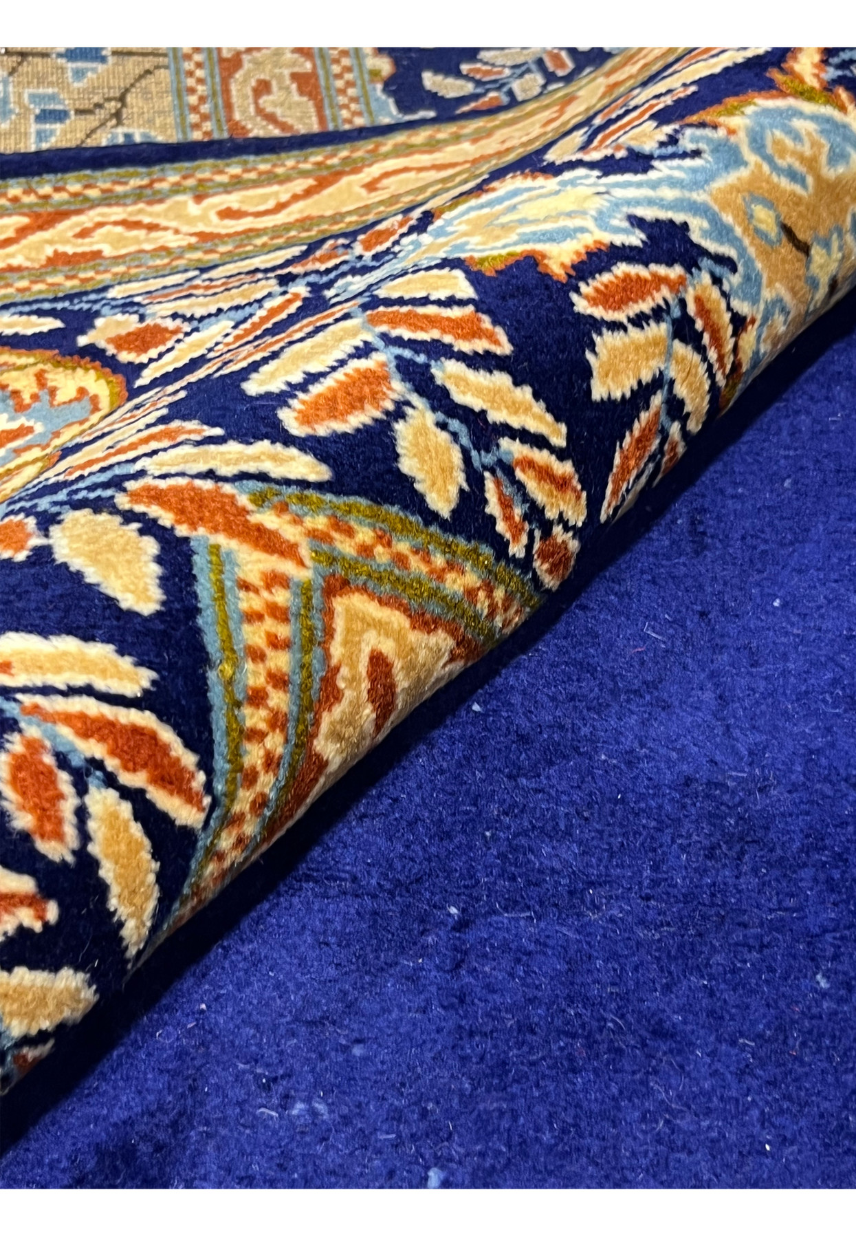 Rolled view of palace-size Persian Yazd rug showing wool pile depth and finely drawn navy border with floral detail
