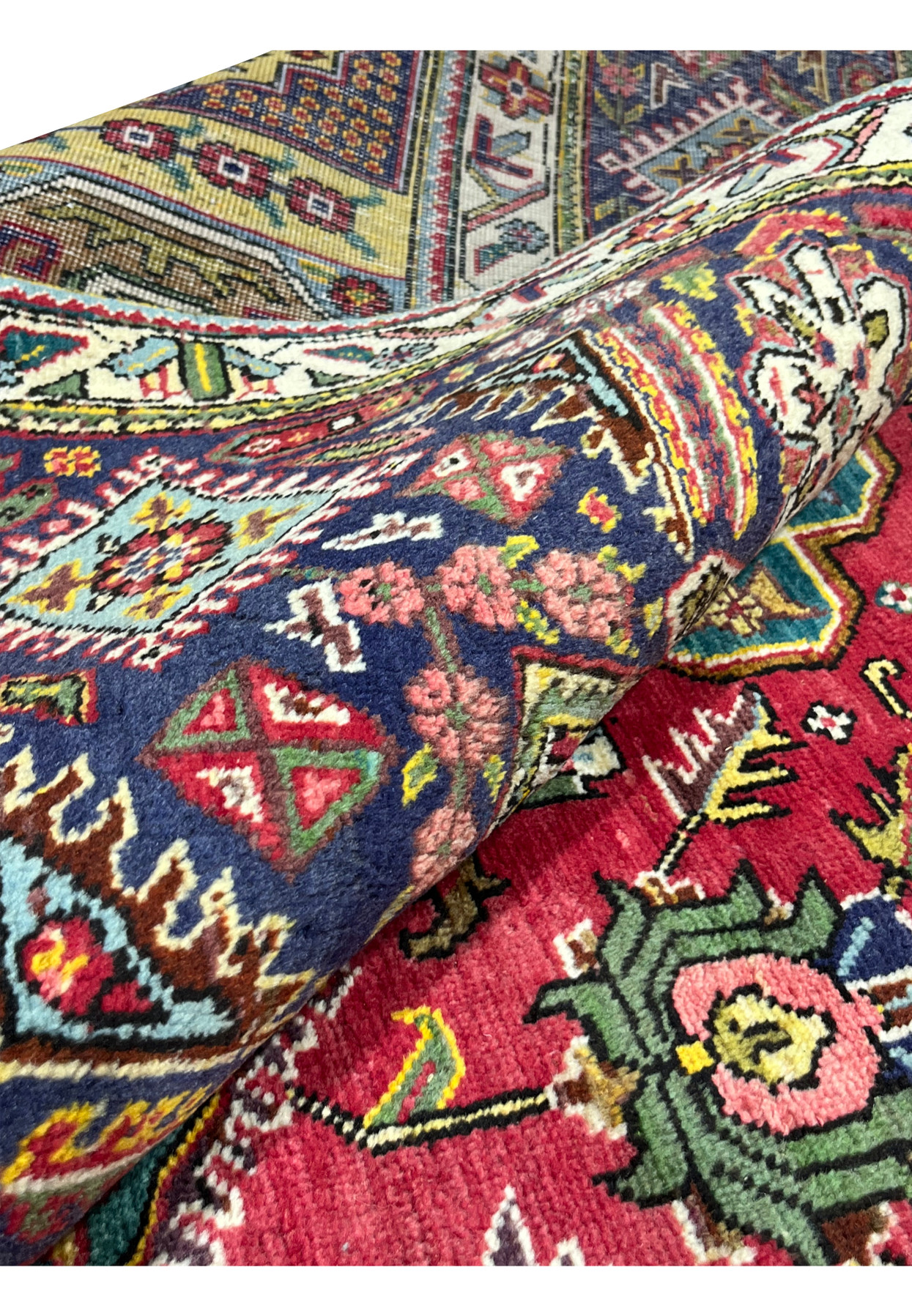 Rolled corner of the Tabriz revealing dense hand-knotted wool pile and vivid red and gold colors