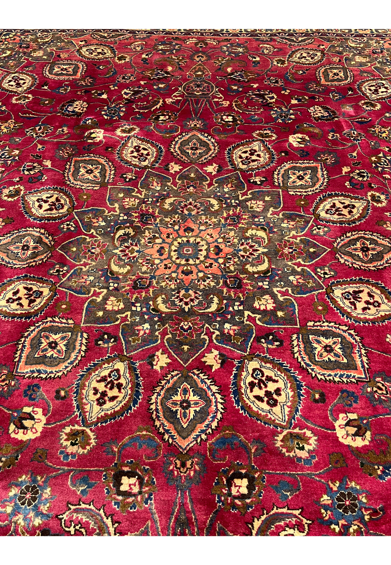 Central floral star medallion of the Persian Mashad in salmon, gold, and indigo on raspberry