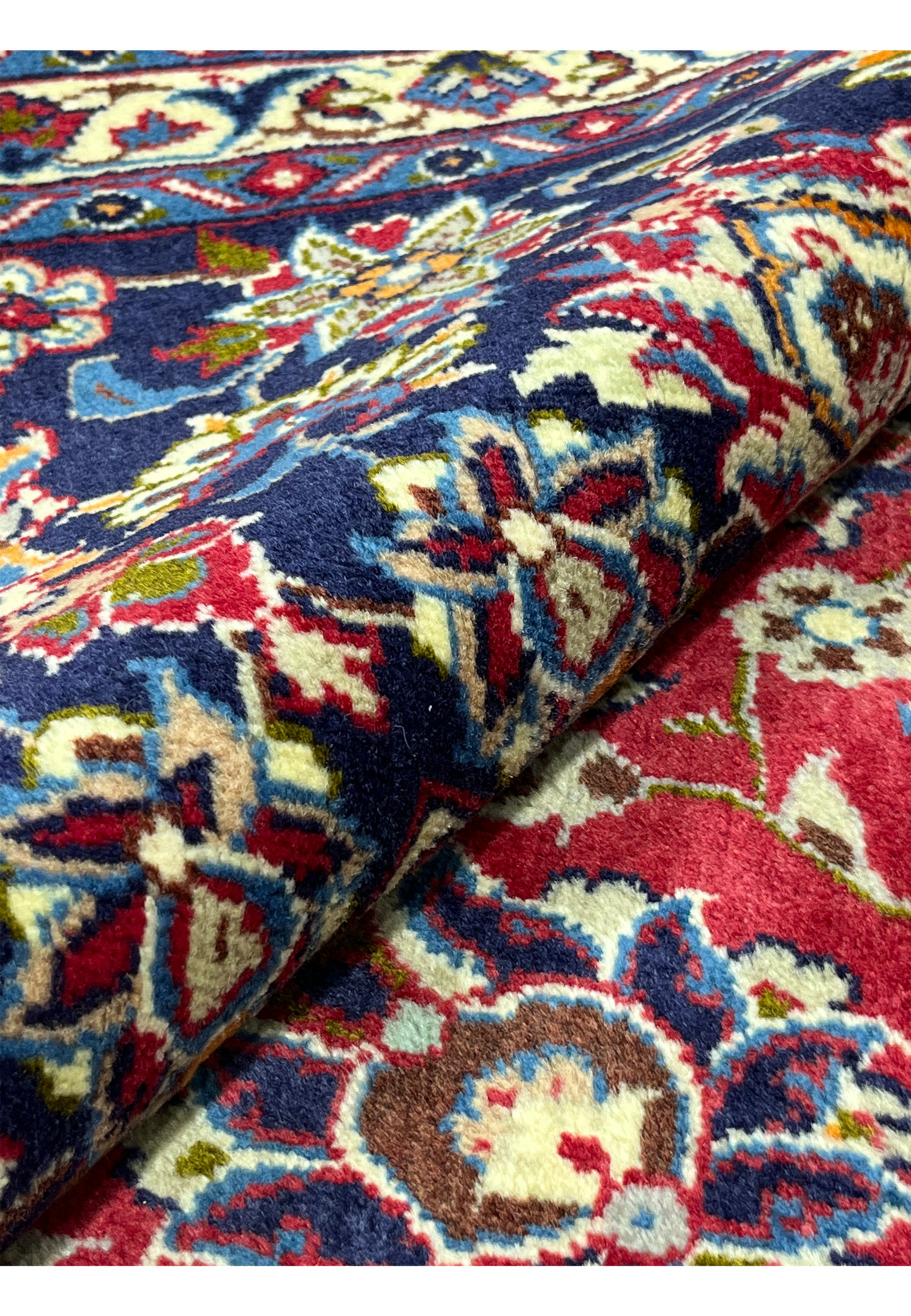 Rolled Persian Najafabad rug revealing the dense even pile and rich red and blue palette