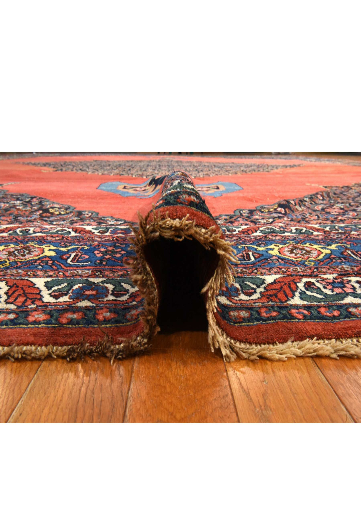 Antique copper-red Bijar folded back to show the navy floral border and woven reverse