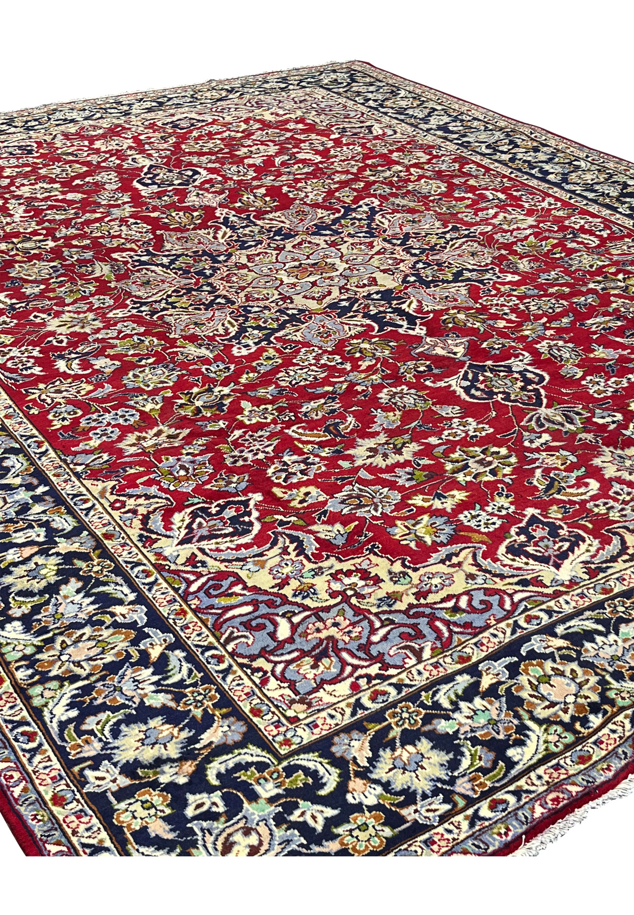 Angled view of this large red Persian floor rug, highlighting the dense floral field and indigo border.