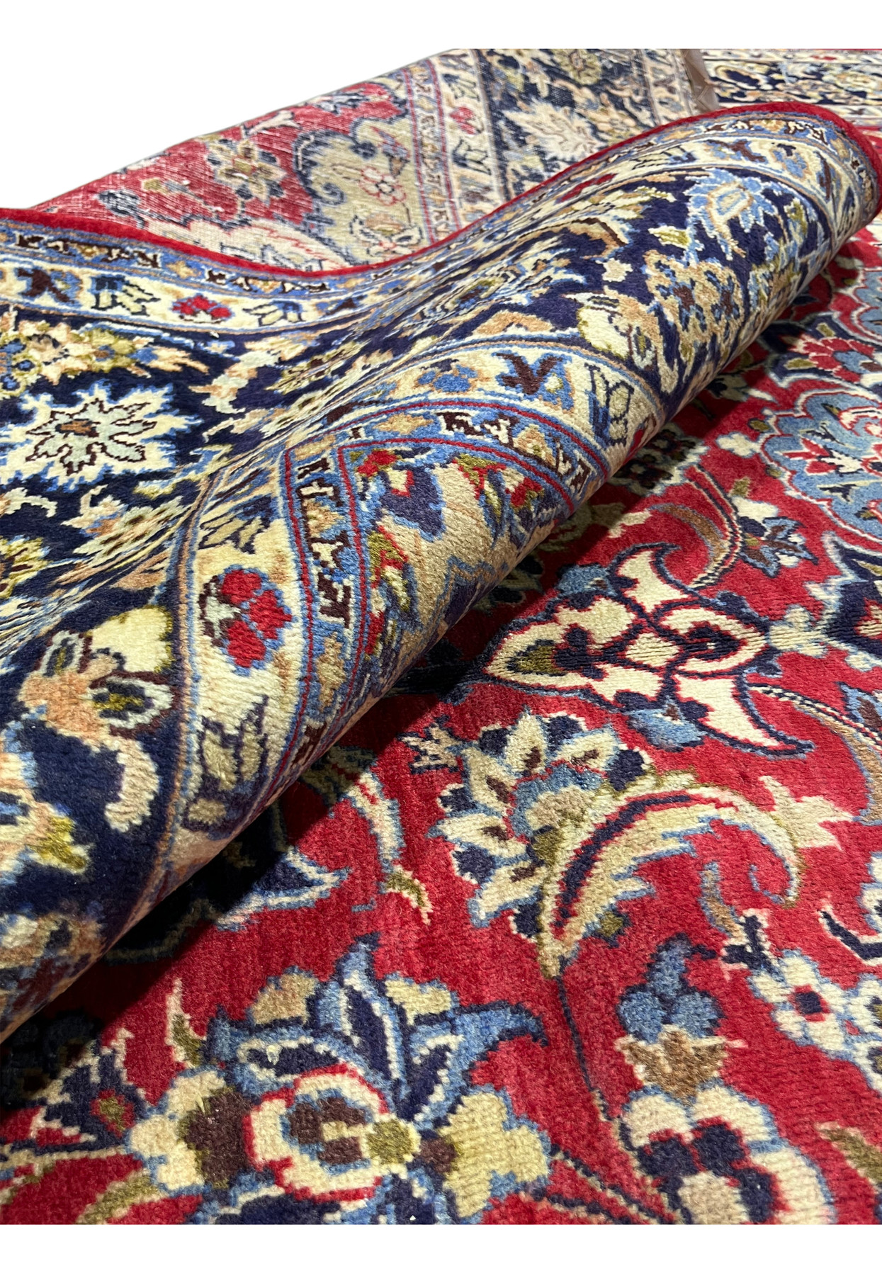 Soft wool pile rolled to show the depth of red, navy, and ivory in this hand-knotted rug.