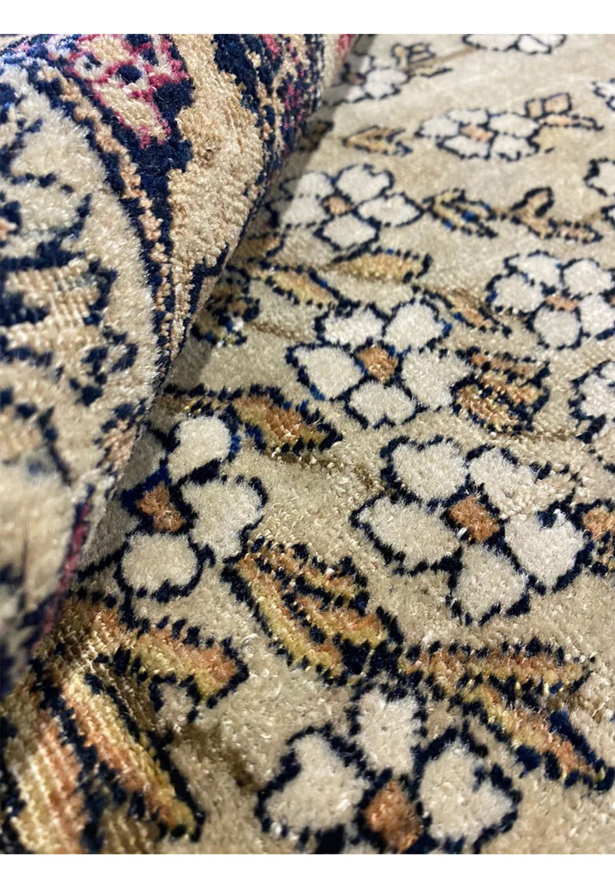 Rolled antique Tehran rug showing wool pile and its age softened coloring.