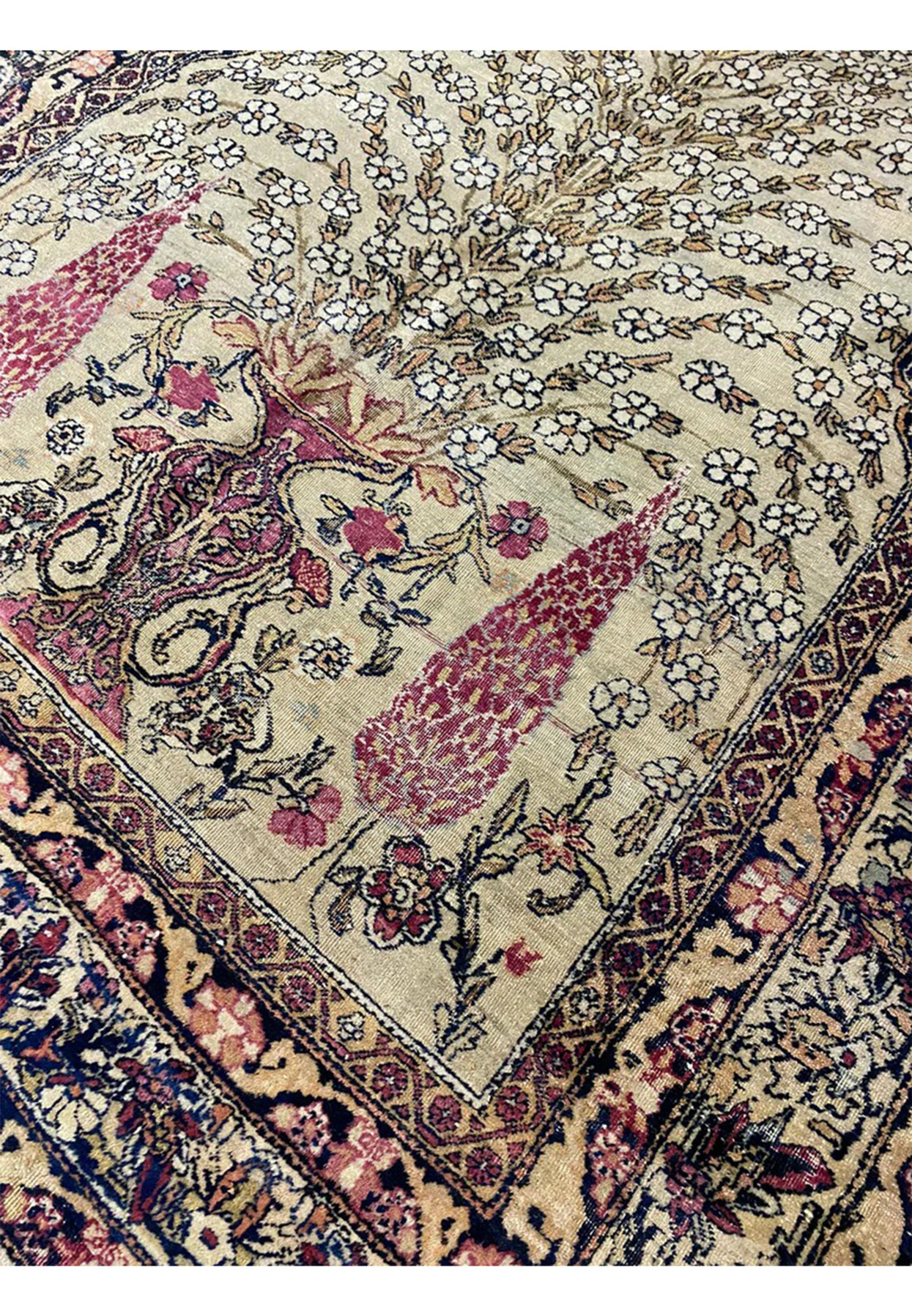 Angled view of the antique Tehran prayer rug showing the softened ivory field and floral border.