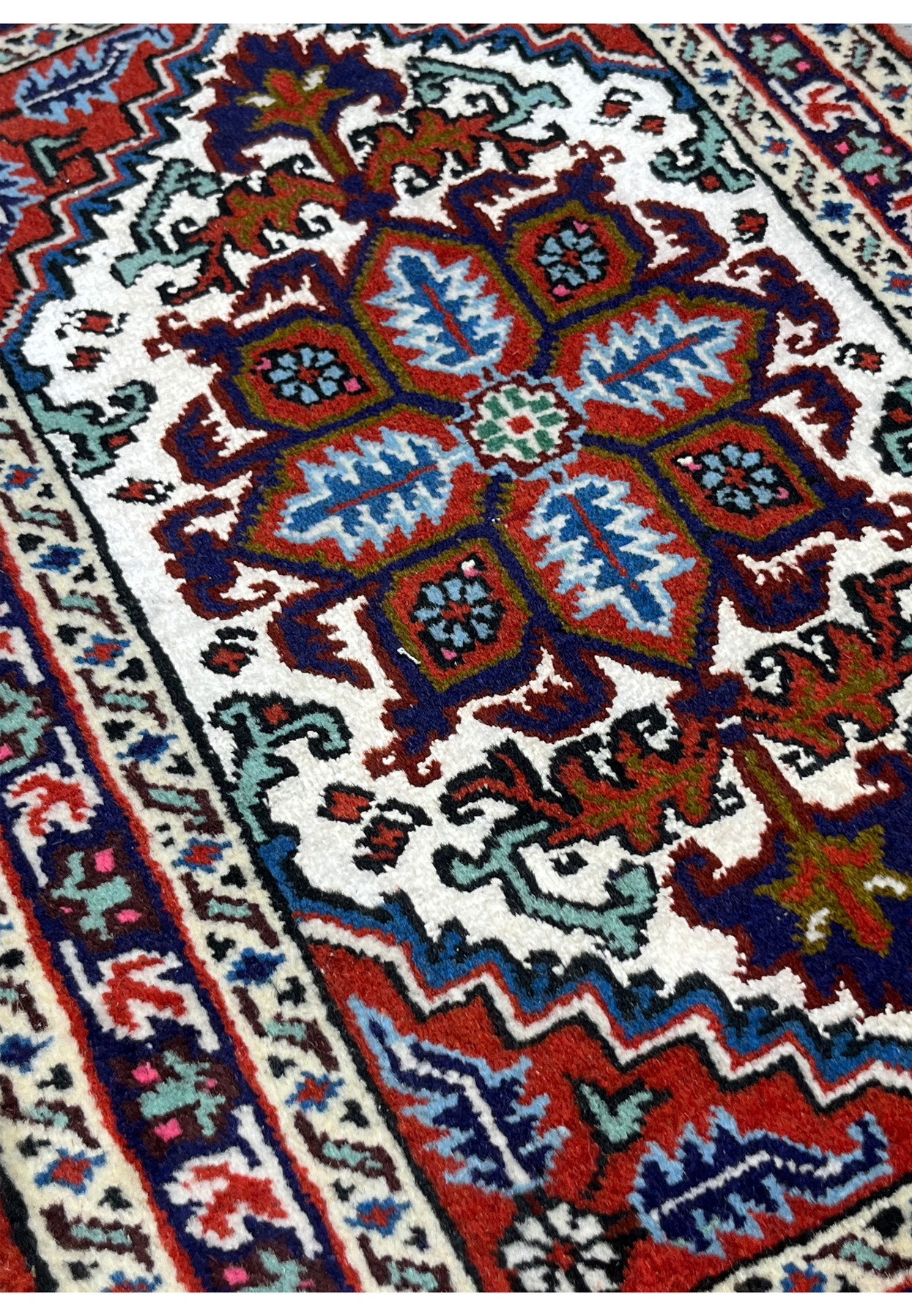 Angled view of bright Ardebil baby rug showing orange red spandrels and mint green border vine