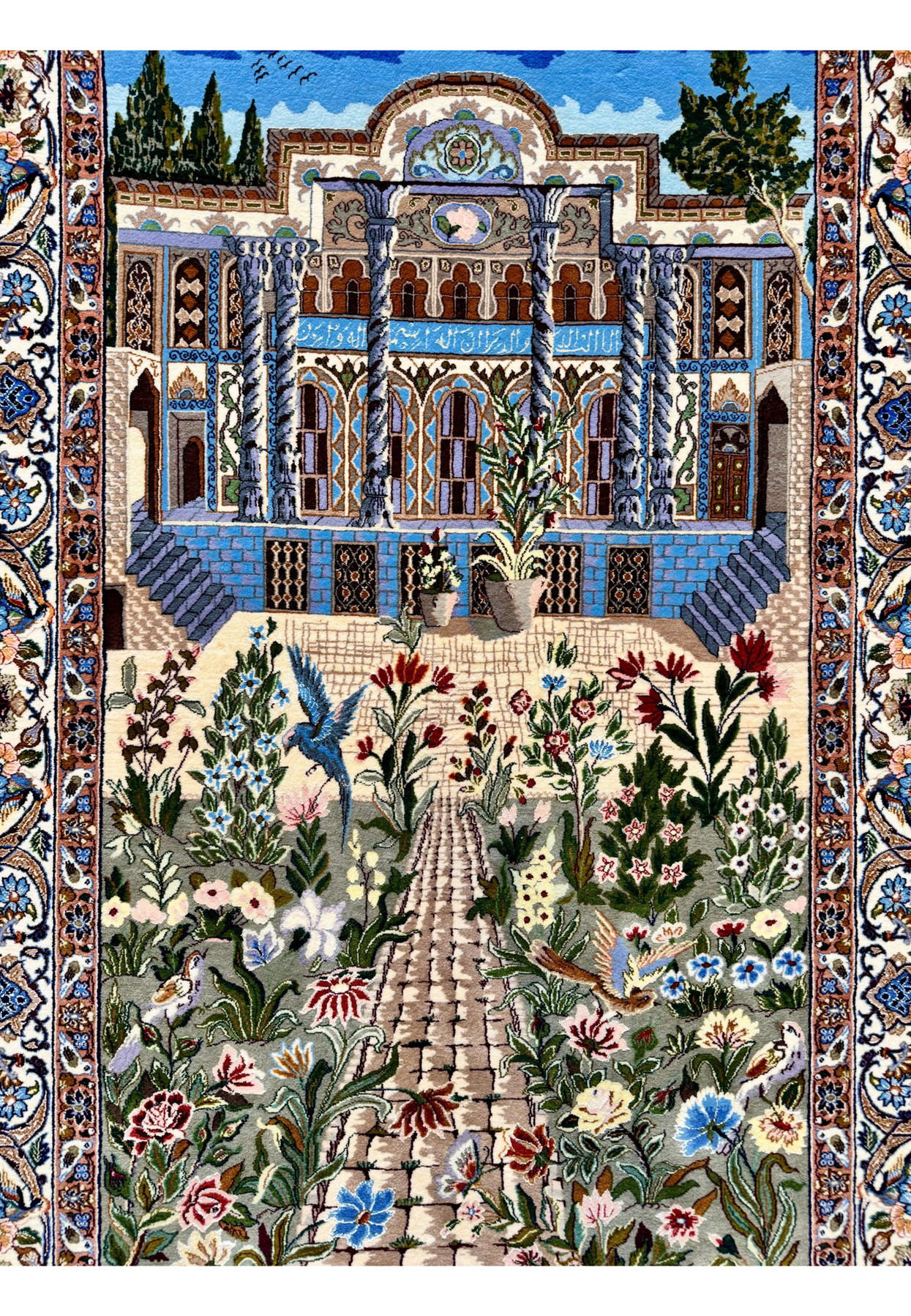 Palace facade with spiral columns and blue tilework rising above a flower filled woven garden