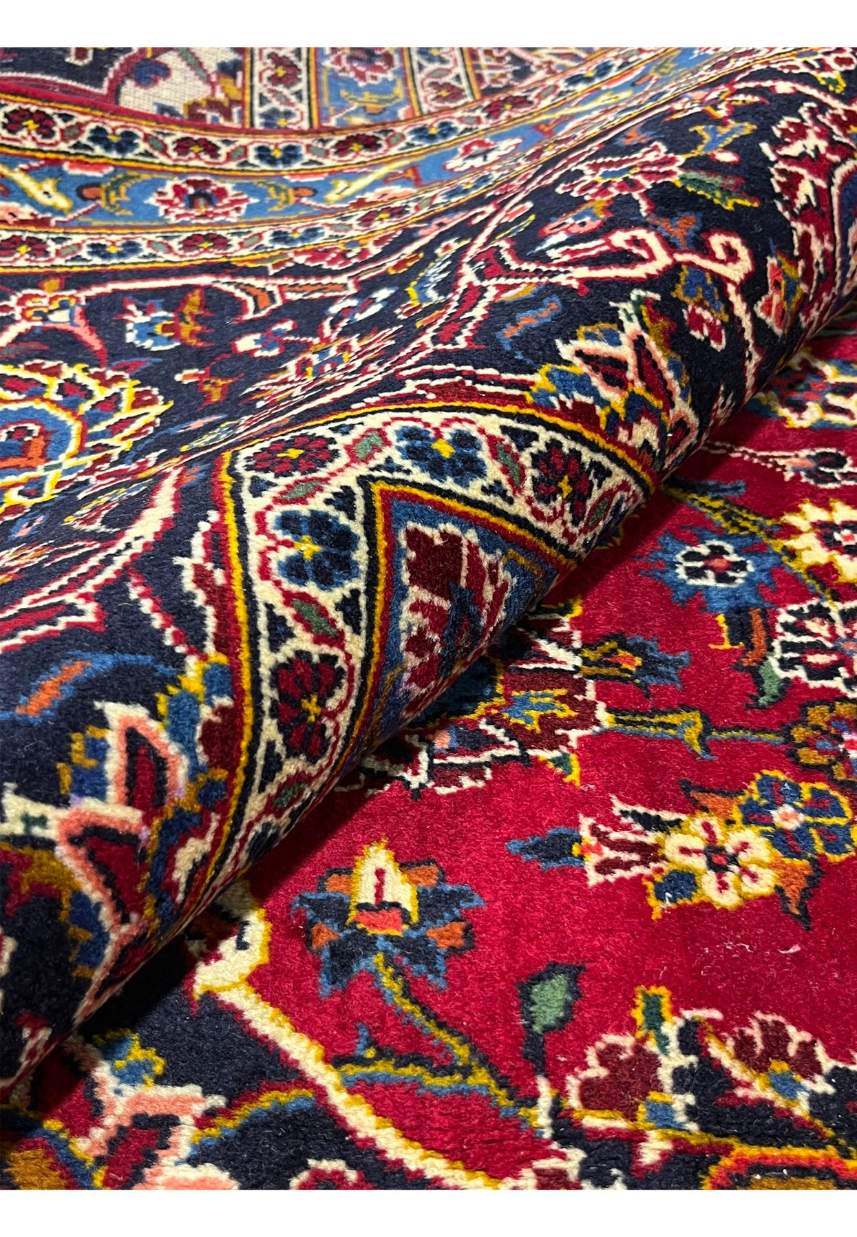 Rug rolled at the border, showing dense wool pile and rich saturated red ground