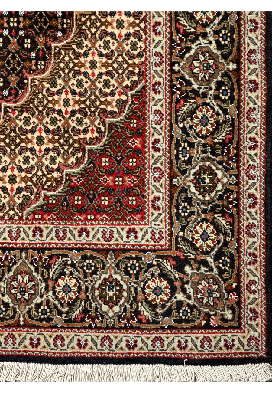 A Persian Tabriz Mahi rug's border detailed with navy blue, olive green, pink, and cream designs on a dark brown background