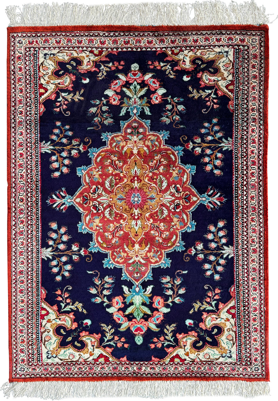 Elegant Persian Qum silk rug with a central floral medallion set against a navy blue background and an ornate border