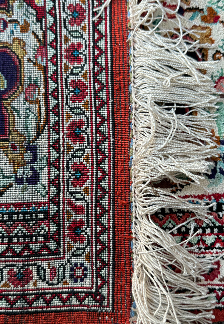 Partial view of a Persian Qum silk rug with a focus on the detailed floral border and fringe