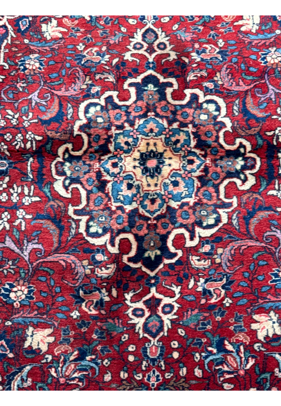 A detailed view of a Persian Sarough rug showcasing the central medallion and surrounding floral motifs in a rich palette of red, blue, and cream