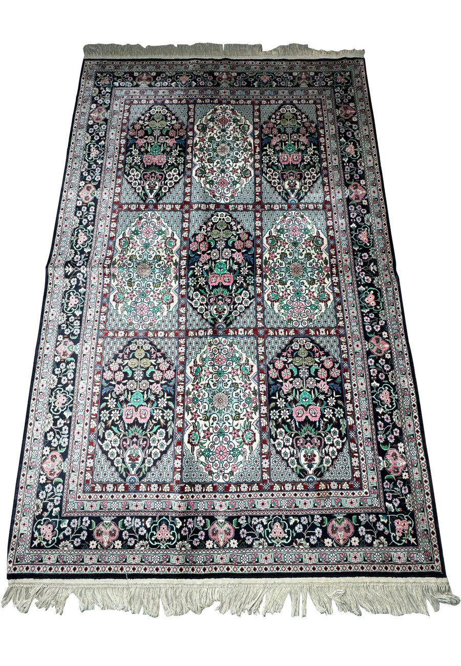 Full view of a Persian Qum silk rug displaying detailed floral designs and a rich color palette on a navy base