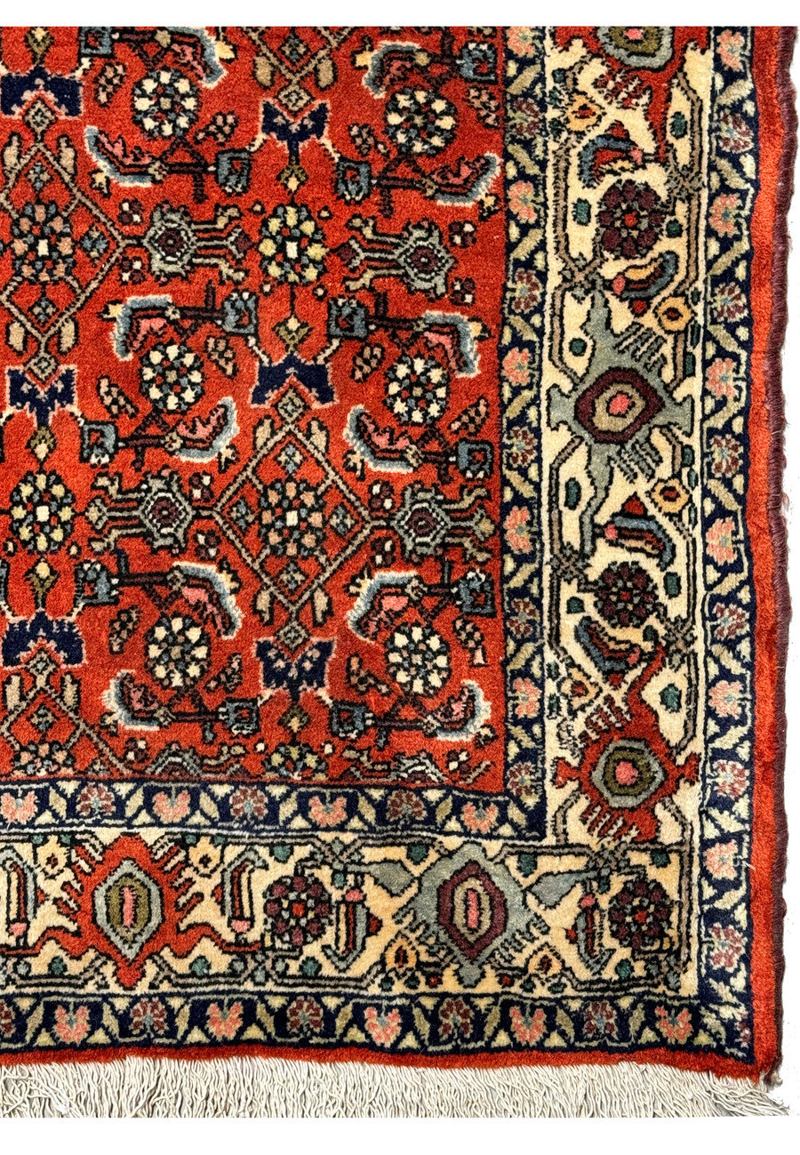 The corner of the vintage Bijar rug showing the border and fringe, alongside the central pattern.